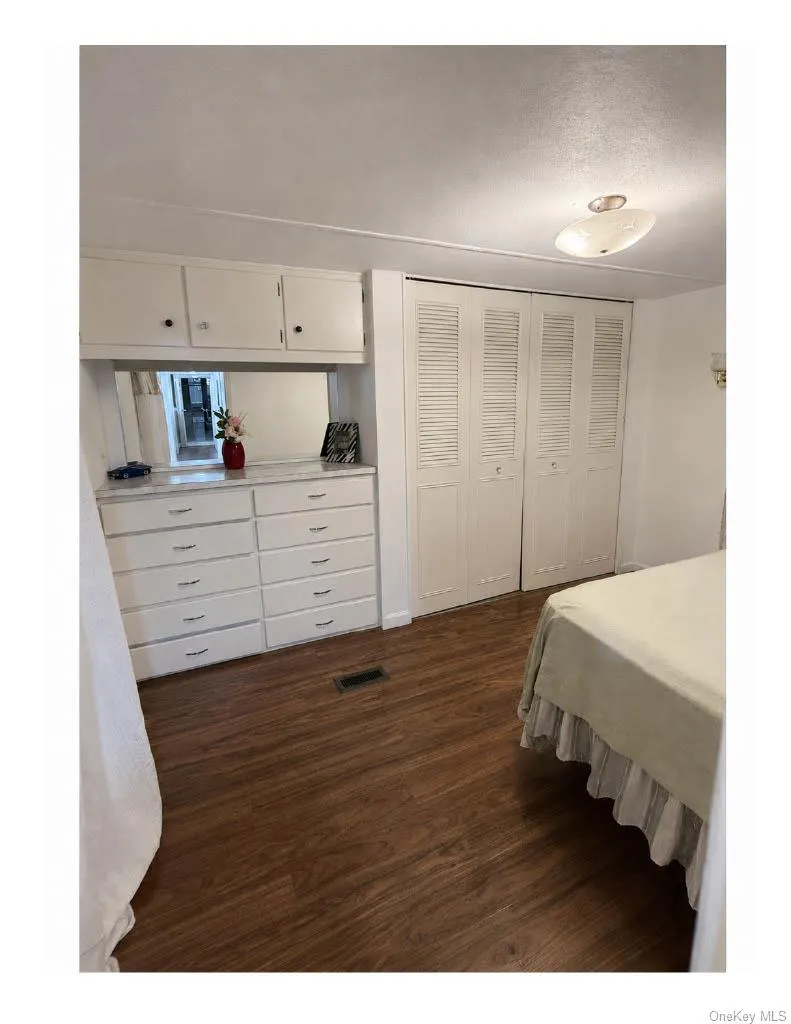 Bedroom 3 Integrated dresser and cabinetry with mirror, wood-finish flooring, white louvered bifold closet doors, and flush-mount ceiling lighting Bedroom 3 Integrated dresser and cabinetry with mirror, wood-finish flooring, white louvered bifold closet doors, and flush-mount ceiling lighting