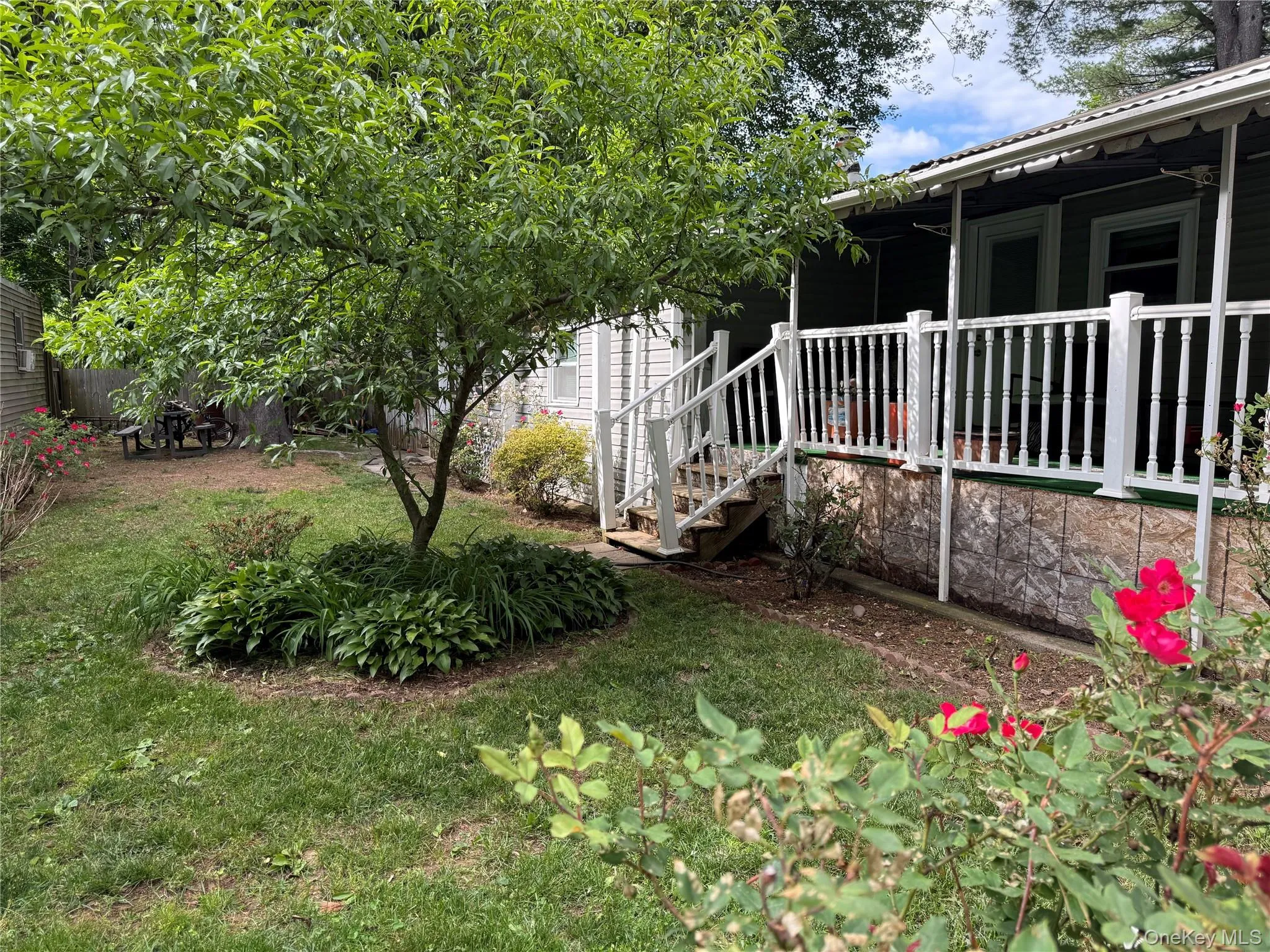 Expansive lawn featuring a mature tree, established garden beds, and red flowering bushes Expansive lawn featuring a mature tree, established garden beds, and red flowering bushes