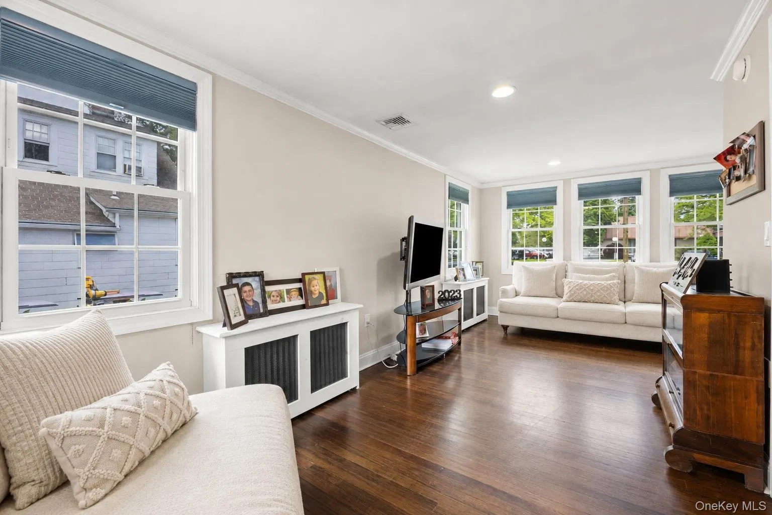 Living area featuring wood-finish flooring, white trim, recessed lighting, and multiple windows with blue cellular shades Living area featuring wood-finish flooring, white trim, recessed lighting, and multiple windows with blue cellular shades