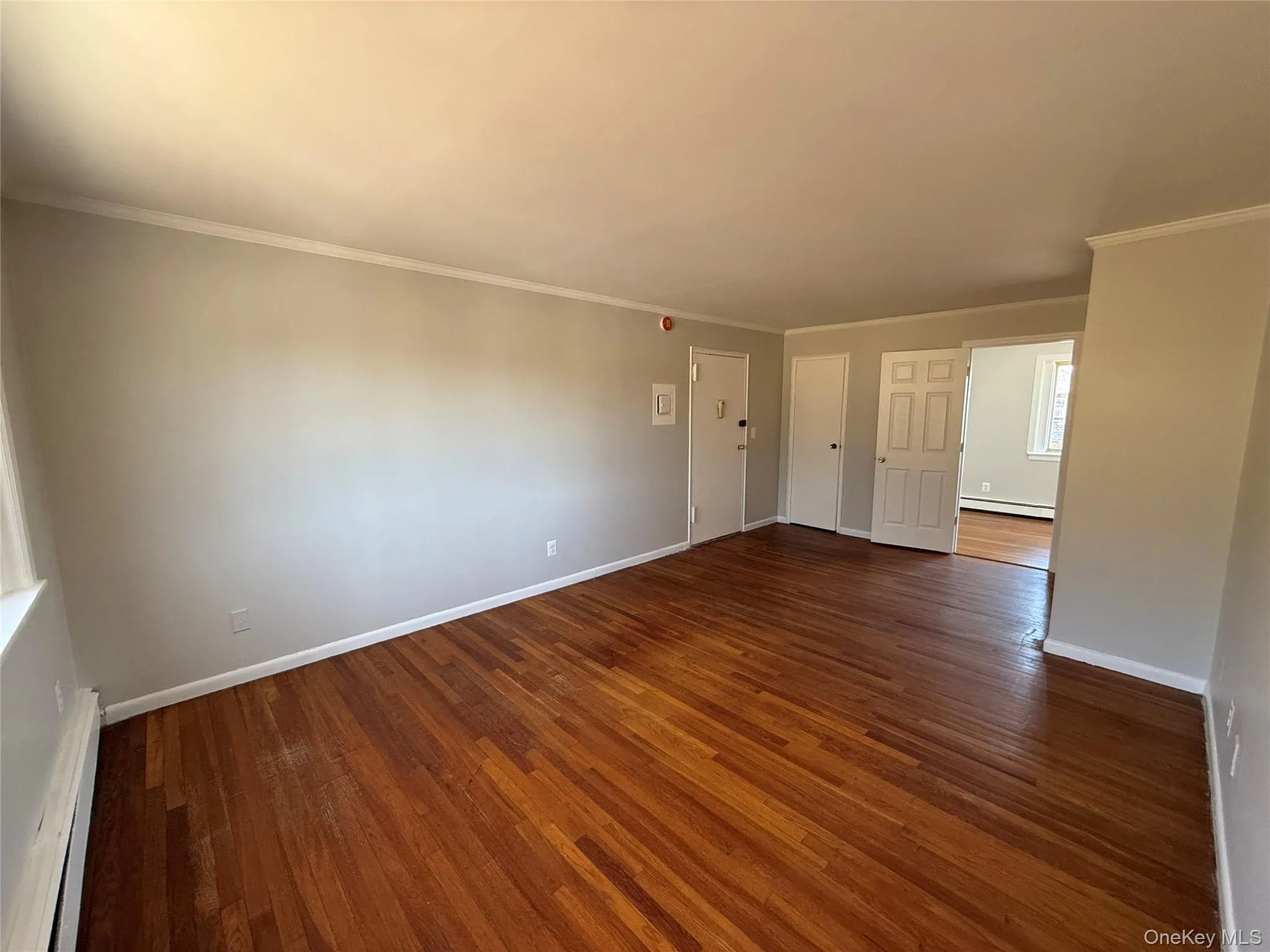 Spare room with a baseboard radiator, a baseboard heating unit, dark wood-style flooring, baseboards, and ornamental molding Spare room with a baseboard radiator, a baseboard heating unit, dark wood-style flooring, baseboards, and ornamental molding