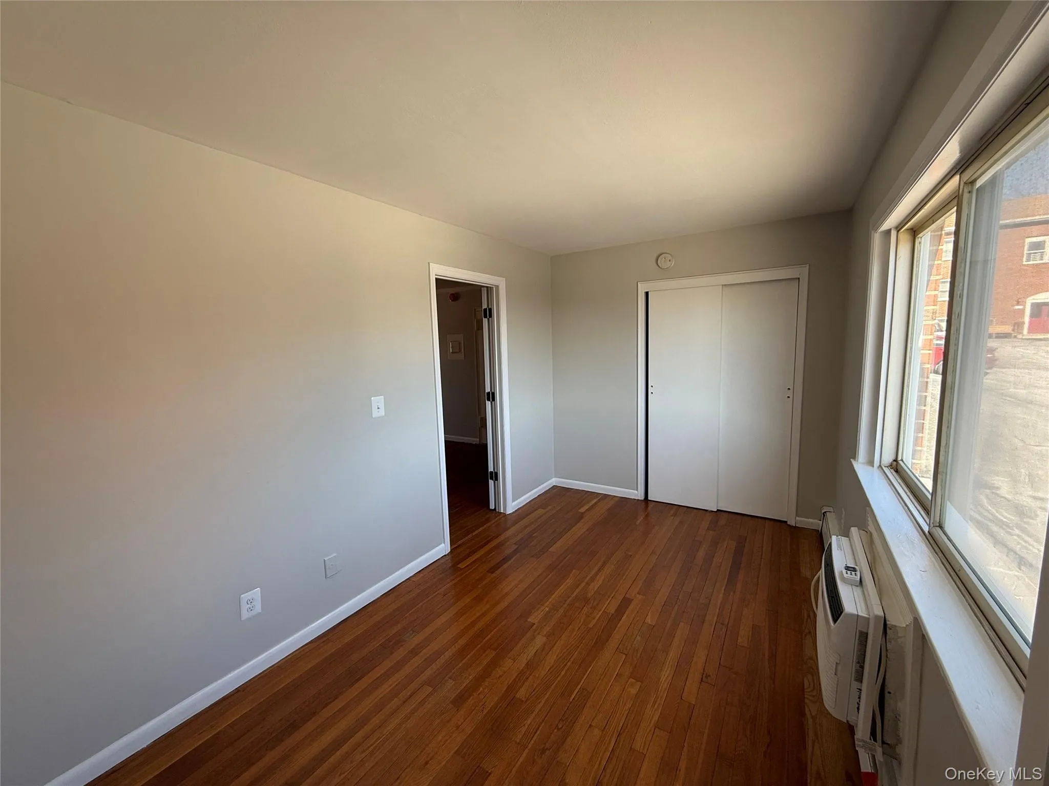 Unfurnished bedroom featuring dark wood-style floors, an AC wall unit, a closet, and baseboards Unfurnished bedroom featuring dark wood-style floors, an AC wall unit, a closet, and baseboards