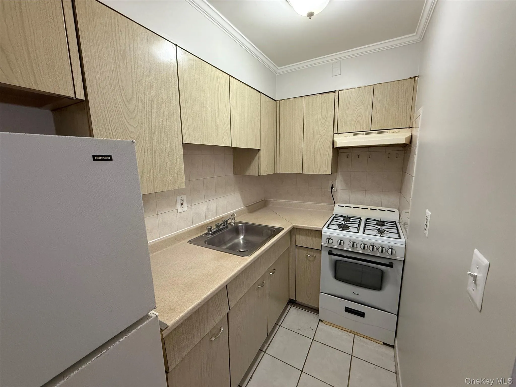 Kitchen with under cabinet range hood, white appliances, a sink, light countertops, and crown molding Kitchen with under cabinet range hood, white appliances, a sink, light countertops, and crown molding