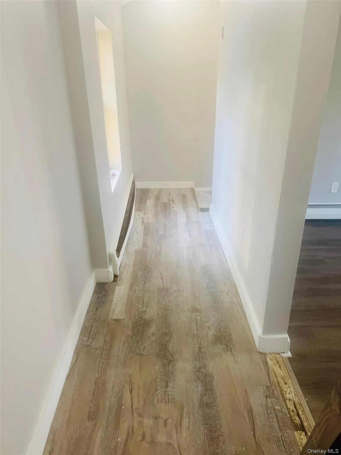 Hallway featuring wood-finish flooring, white baseboards, and light-toned wall paint Hallway featuring wood-finish flooring, white baseboards, and light-toned wall paint