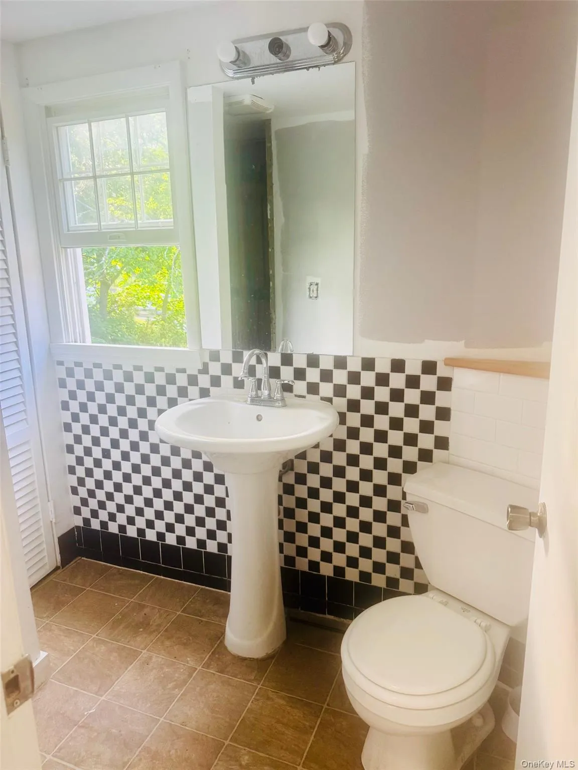 Bathroom featuring a pedestal sink, checkered wall tiling, and a window with natural light, with a new shower being installed Bathroom featuring a pedestal sink, checkered wall tiling, and a window with natural light, with a new shower being installed