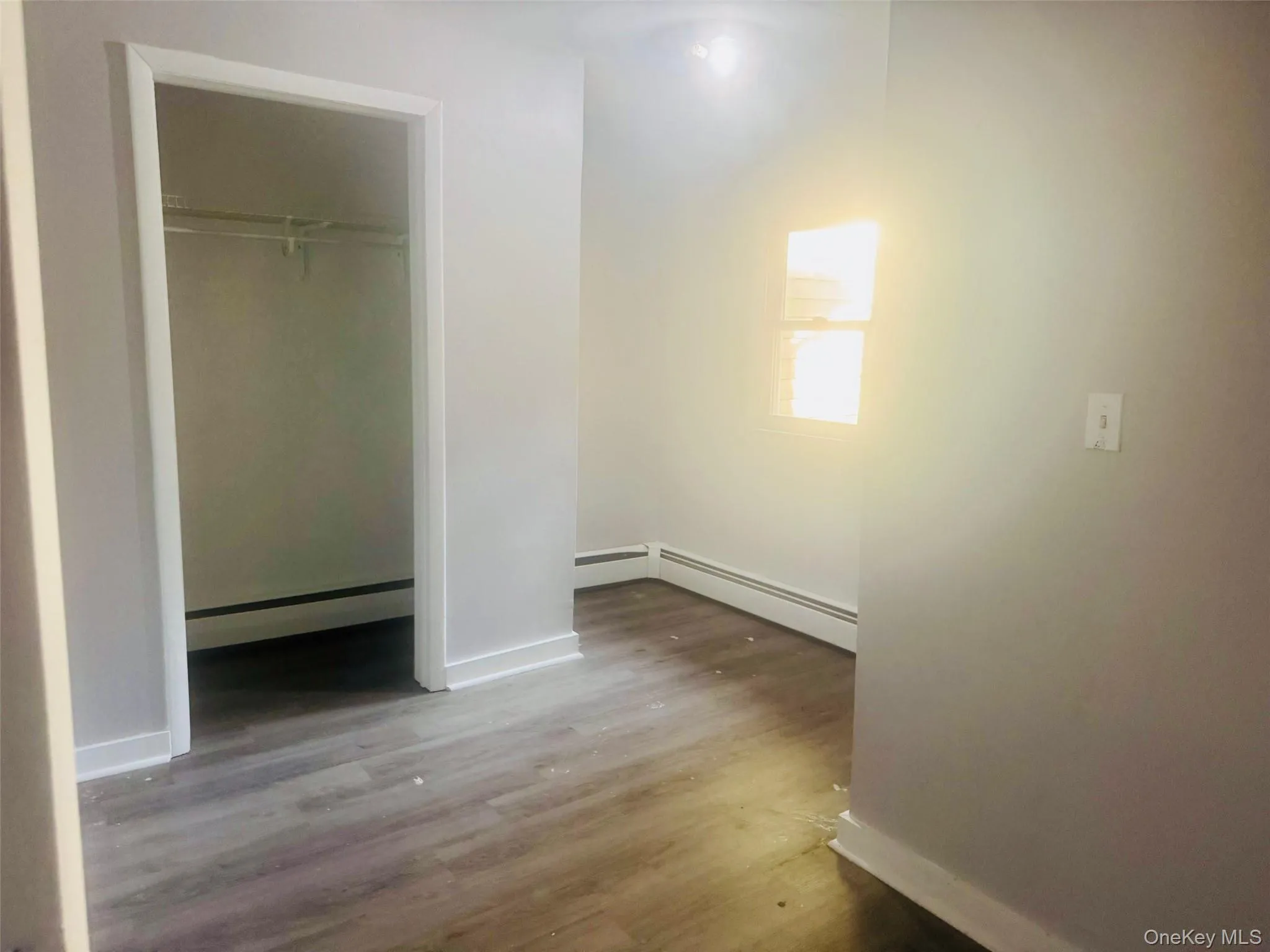 Bedroom featuring wood-finish flooring, light grey painted walls, white trim, and a window with blinds Bedroom featuring wood-finish flooring, light grey painted walls, white trim, and a window with blinds