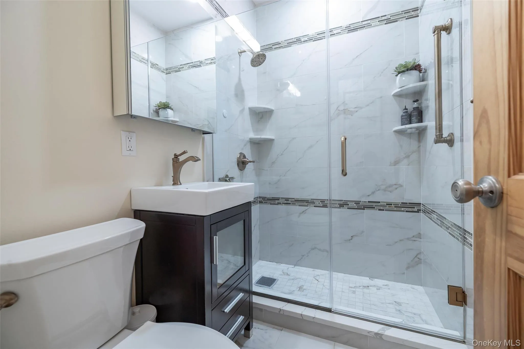 Bathroom featuring a glass-enclosed shower with white marble-patterned tile, a mosaic tile accent band, and integrated shelving Bathroom featuring a glass-enclosed shower with white marble-patterned tile, a mosaic tile accent band, and integrated shelving