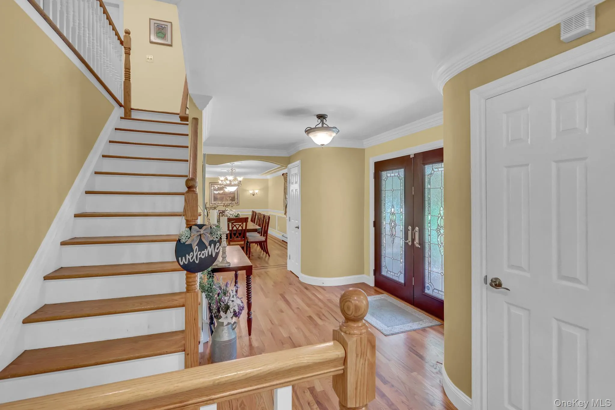 Entry foyer featuring hardwood flooring, a grand staircase with wood treads and white risers, decorative glass double entry doors, a curved wall, and crown molding Entry foyer featuring hardwood flooring, a grand staircase with wood treads and white risers, decorative glass double entry doors, a curved wall, and crown molding