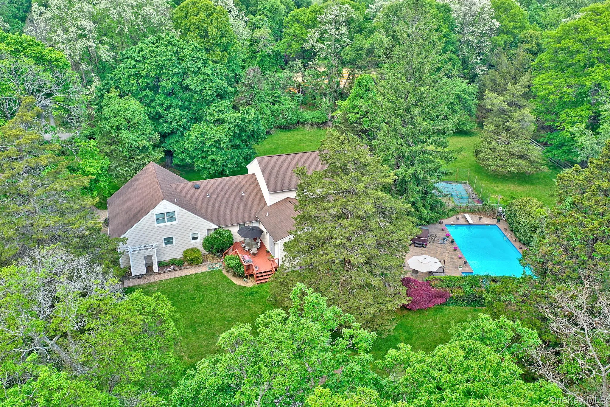 Expansive property featuring a multi-level home with a private swimming pool, surrounding patio, and a dedicated sports court Expansive property featuring a multi-level home with a private swimming pool, surrounding patio, and a dedicated sports court