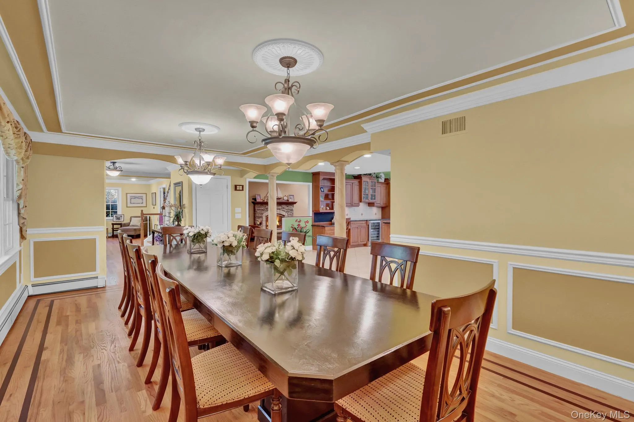 Spacious dining area featuring hardwood flooring with contrasting inlay, decorative wainscoting, crown molding, and two ceiling-mounted light fixtures with medallion details Spacious dining area featuring hardwood flooring with contrasting inlay, decorative wainscoting, crown molding, and two ceiling-mounted light fixtures with medallion details