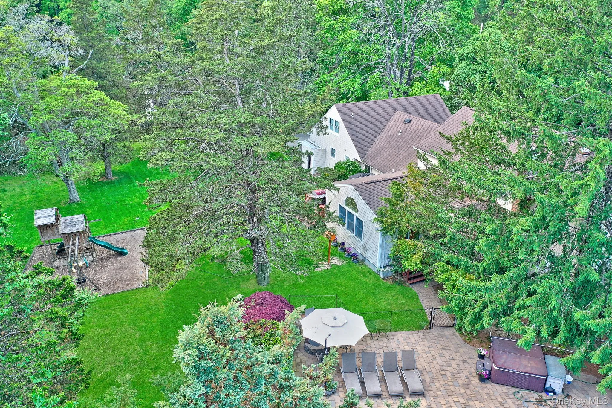 Expansive property featuring a multi-level residence with a large paved patio, outdoor seating area with umbrella, and a built-in spa Expansive property featuring a multi-level residence with a large paved patio, outdoor seating area with umbrella, and a built-in spa