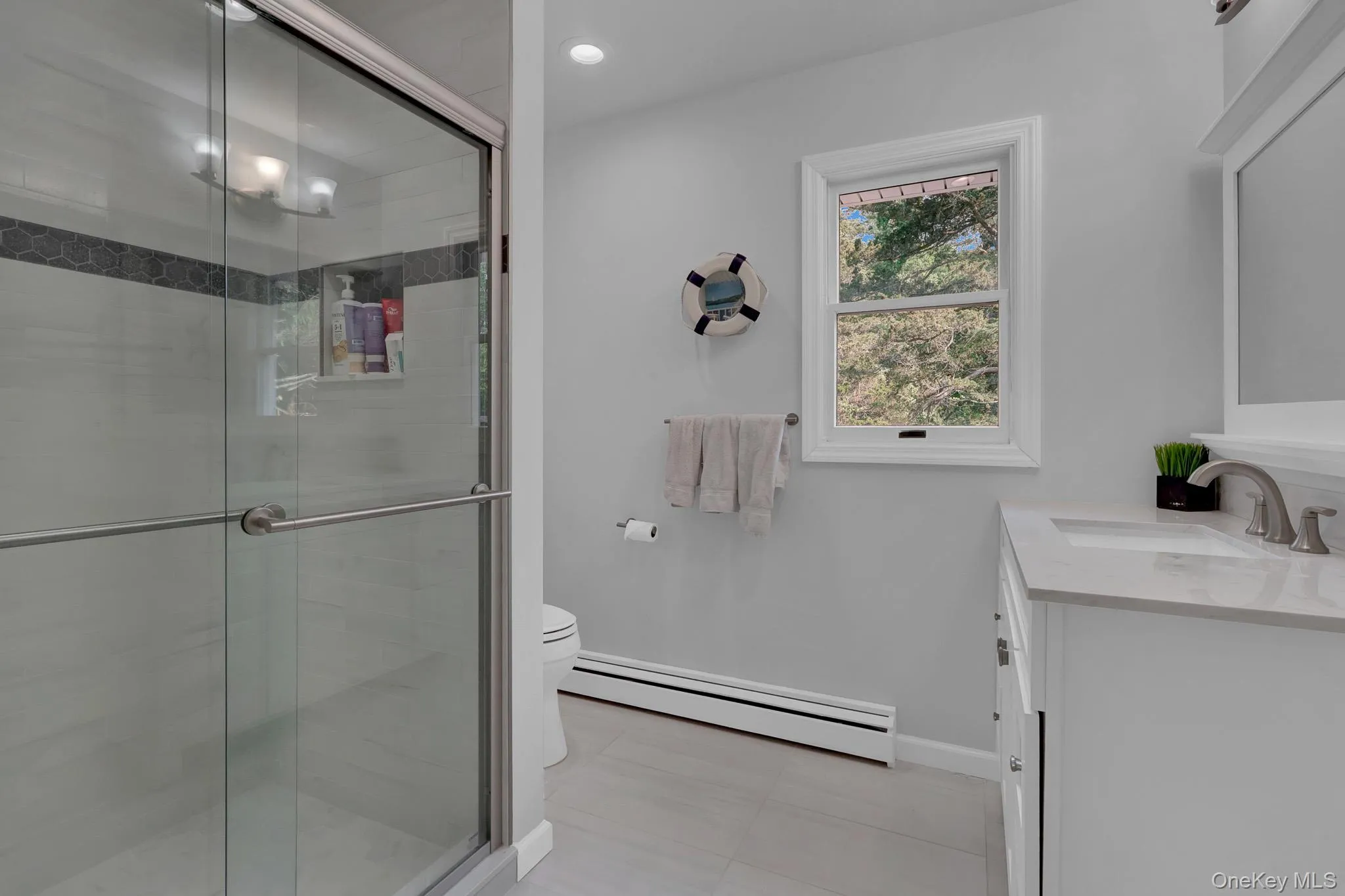 Bathroom featuring a glass-enclosed shower with tile surround and hexagon accent, single vanity with integrated sink and chrome faucet, single window, and a wall-mounted mirror Bathroom featuring a glass-enclosed shower with tile surround and hexagon accent, single vanity with integrated sink and chrome faucet, single window, and a wall-mounted mirror