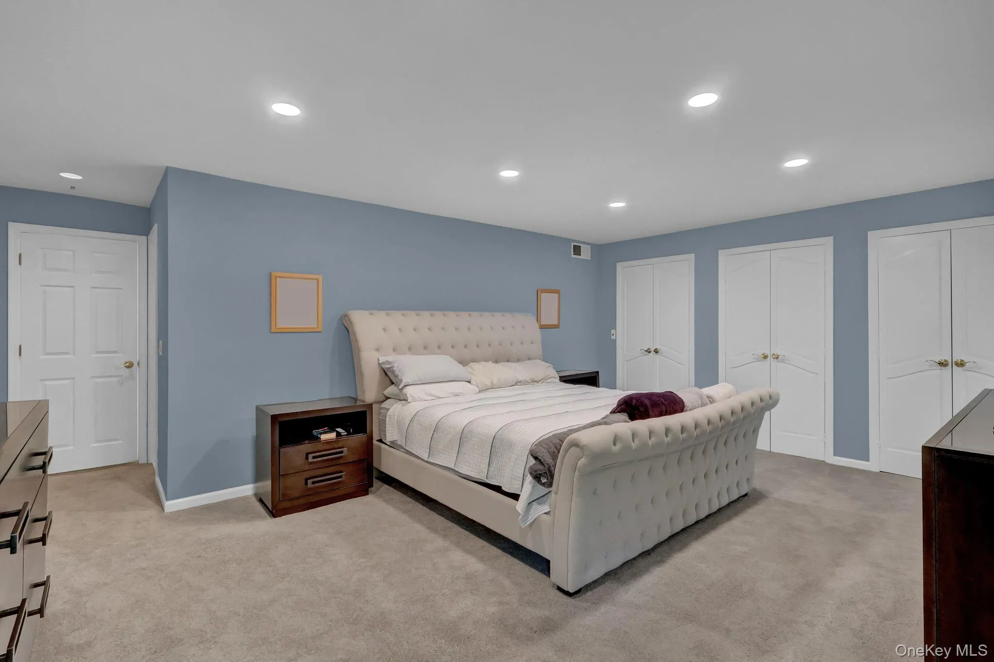 Carpeted room featuring recessed lighting, a neutral wall color, and multiple white bi-fold closet doors Carpeted room featuring recessed lighting, a neutral wall color, and multiple white bi-fold closet doors