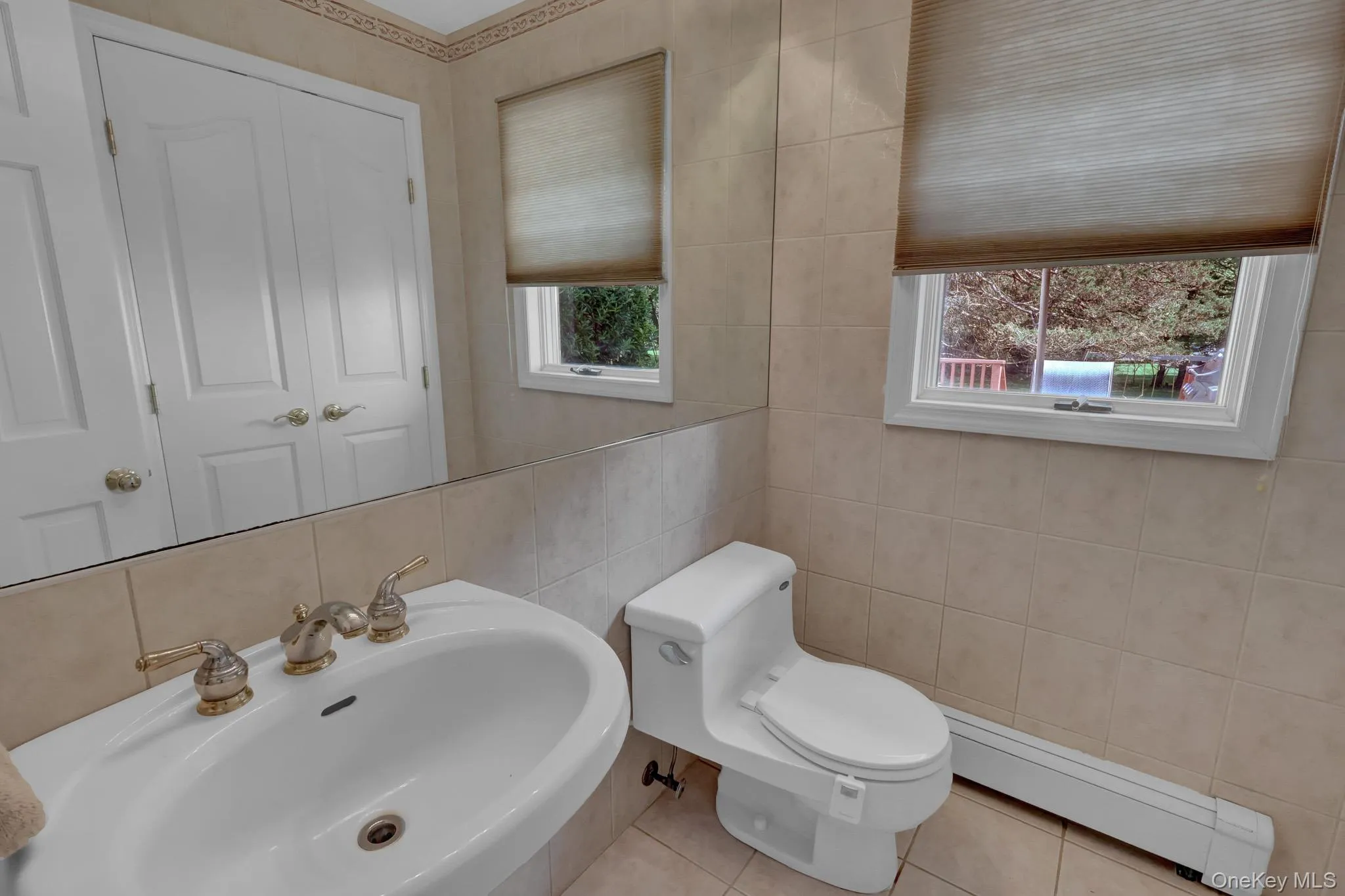 Pedestal sink with brass-finish faucet, full vanity mirror, and neutral-toned wall tile Pedestal sink with brass-finish faucet, full vanity mirror, and neutral-toned wall tile