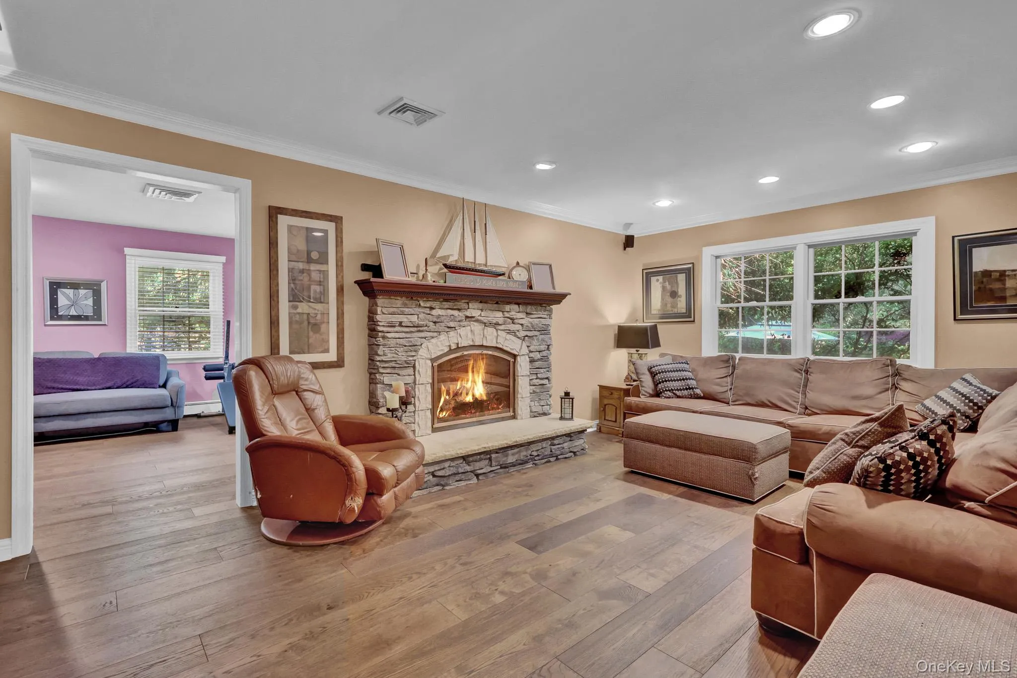 Living area featuring a stone fireplace with hearth, recessed lighting, and wood-finish flooring Living area featuring a stone fireplace with hearth, recessed lighting, and wood-finish flooring