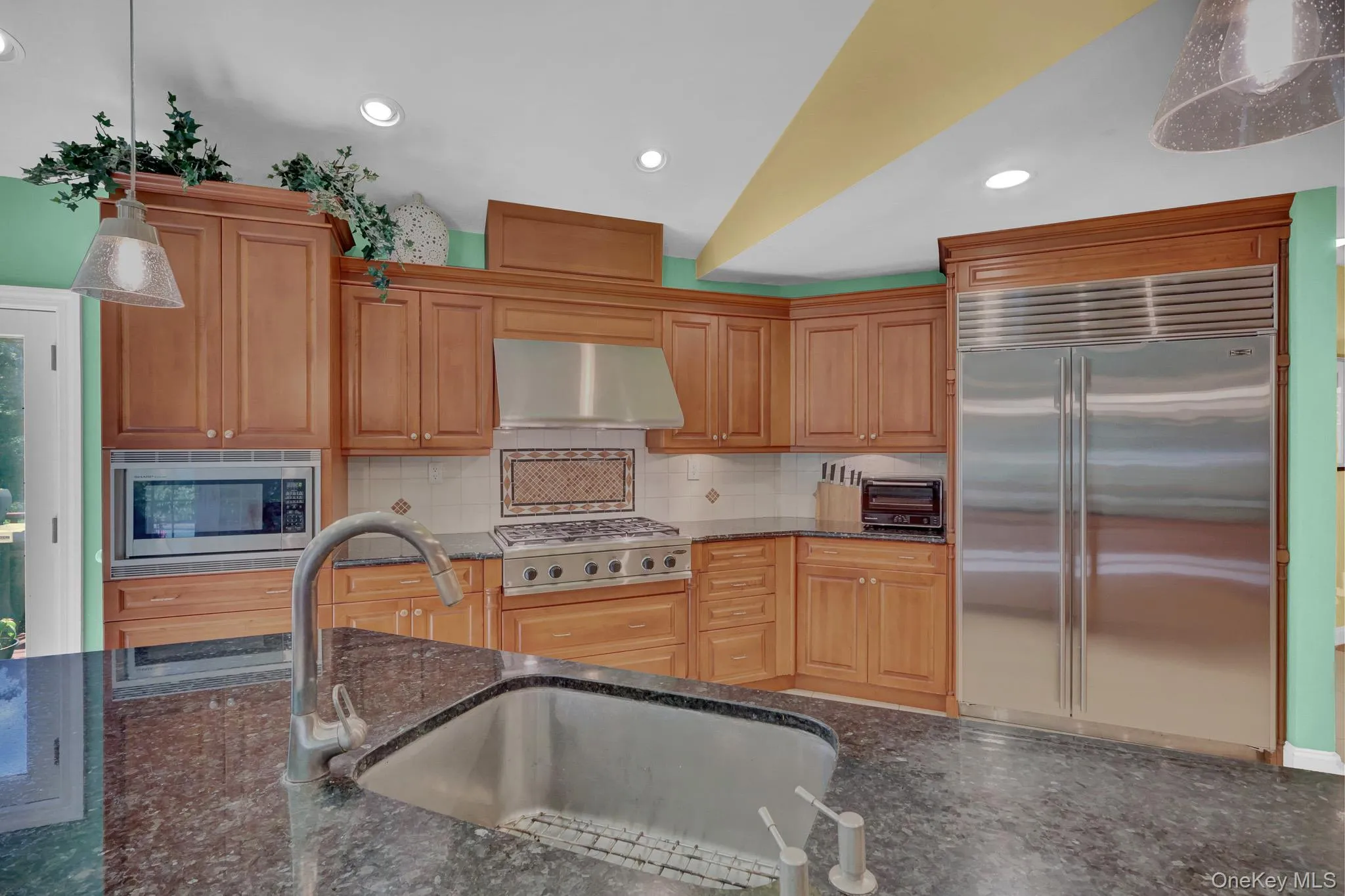 Kitchen featuring rich wood cabinetry, patterned backsplash tile, stainless steel appliances, and dark speckled countertops Kitchen featuring rich wood cabinetry, patterned backsplash tile, stainless steel appliances, and dark speckled countertops