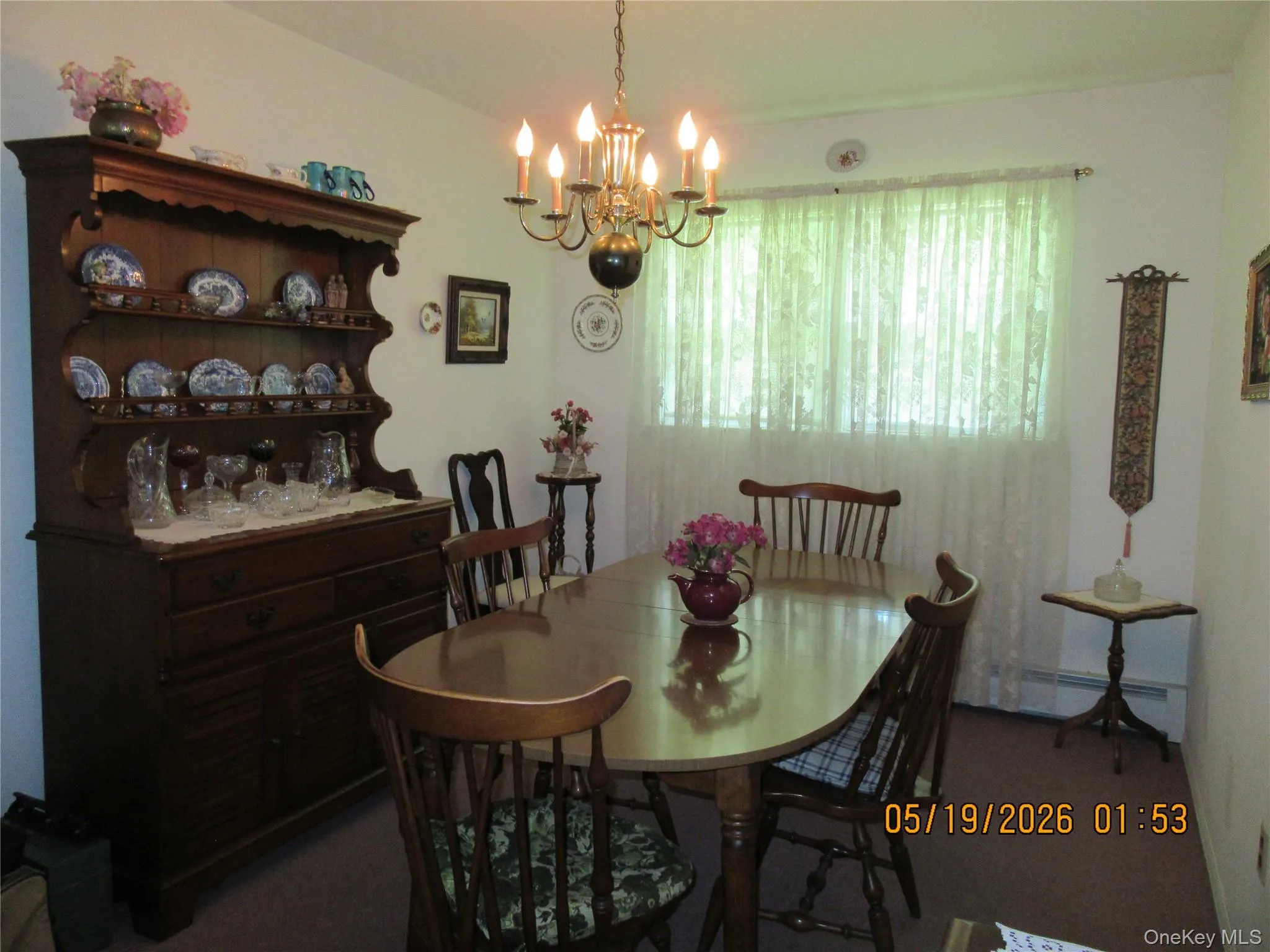 Dining area featuring a central chandelier, a large window, white walls, and carpet flooring Dining area featuring a central chandelier, a large window, white walls, and carpet flooring