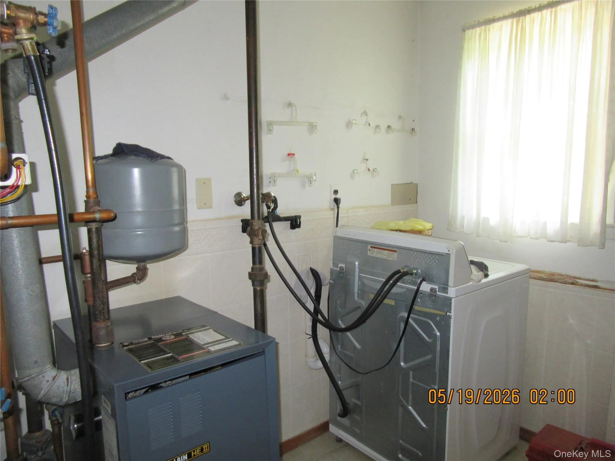 Utility area featuring a floor-standing boiler system with copper piping, a pressure tank, and light-colored wall tiling Utility area featuring a floor-standing boiler system with copper piping, a pressure tank, and light-colored wall tiling