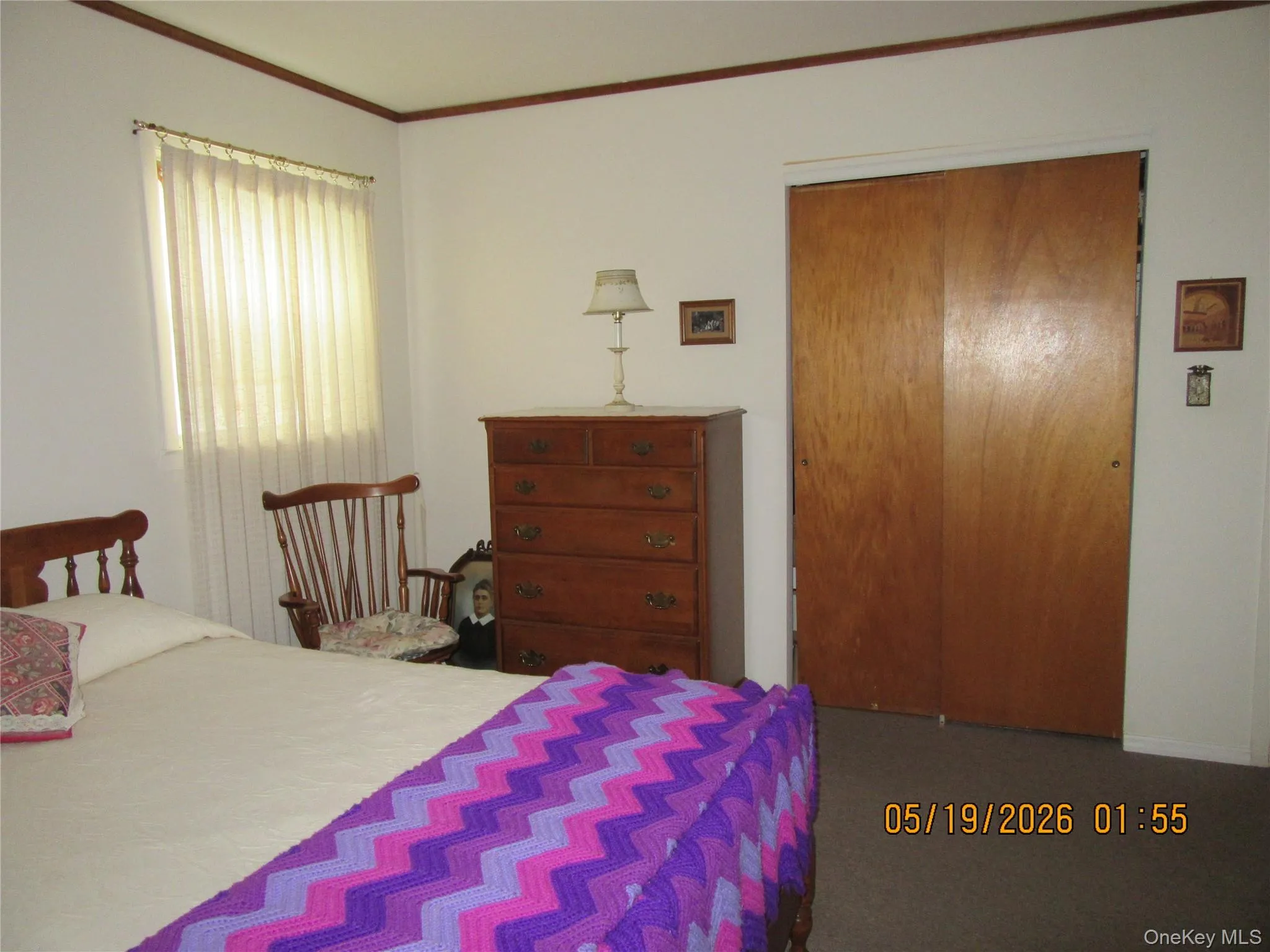 Bedroom featuring a window with sheer curtains, a built-in closet with bi-fold doors, and neutral carpeting Bedroom featuring a window with sheer curtains, a built-in closet with bi-fold doors, and neutral carpeting
