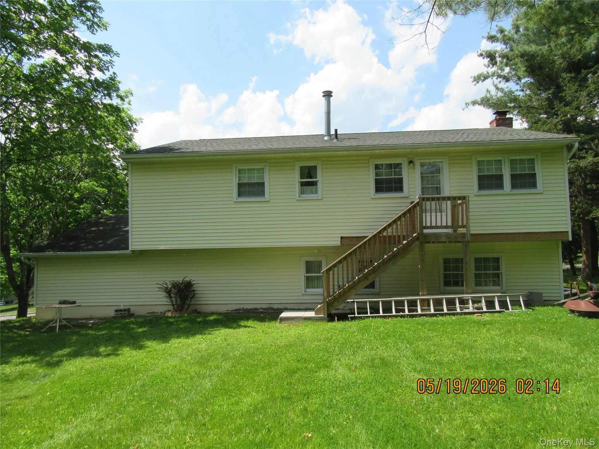 Rear exterior featuring light-colored siding, a wooden deck with stairs, multiple windows, and a foundation Rear exterior featuring light-colored siding, a wooden deck with stairs, multiple windows, and a foundation
