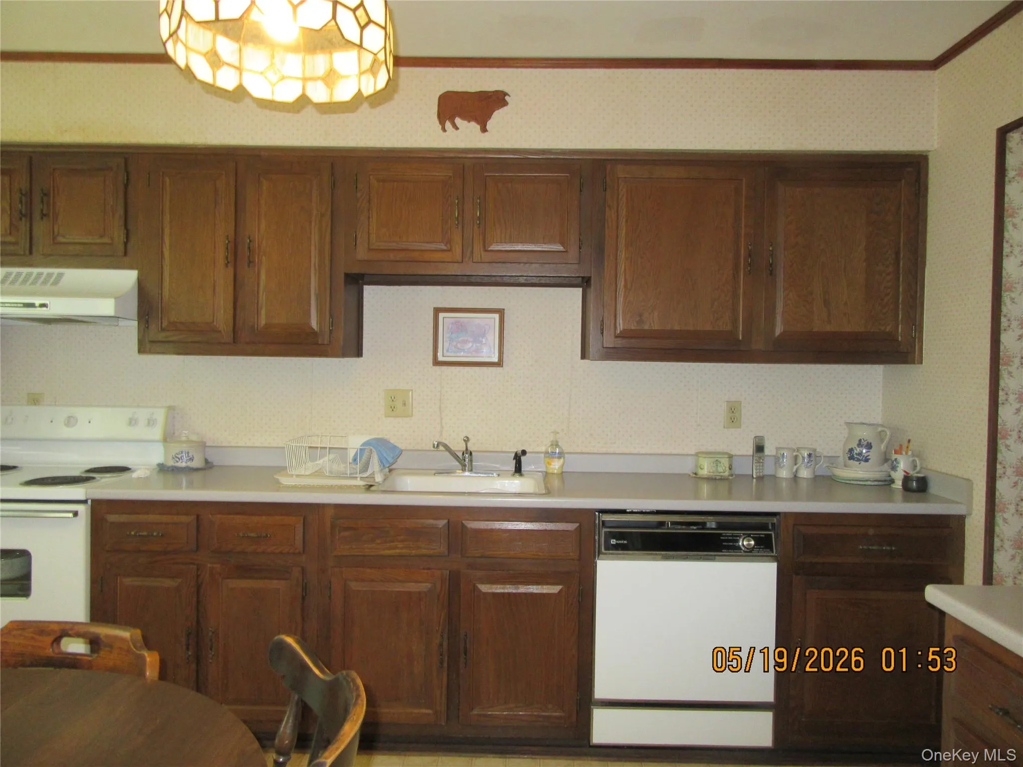 Kitchen featuring wood-finish cabinetry, white countertops, a white range with overhead vent, and an integrated white dishwasher Kitchen featuring wood-finish cabinetry, white countertops, a white range with overhead vent, and an integrated white dishwasher