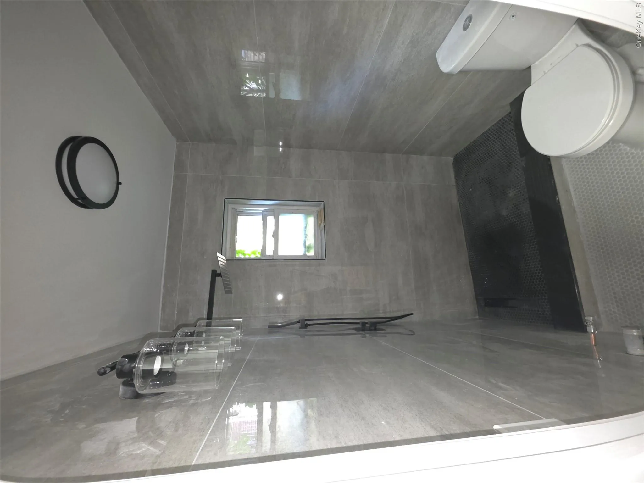 Bathroom featuring gray wall tile, a window, a flush mount ceiling light, and a toilet. Bathroom featuring gray wall tile, a window, a flush mount ceiling light, and a toilet.