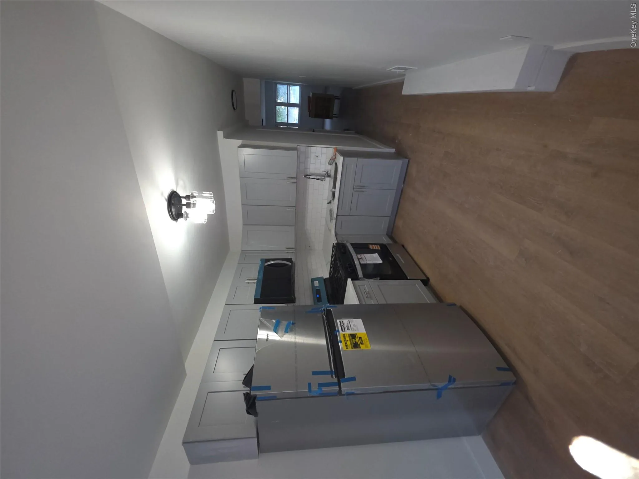 Kitchen featuring light gray cabinetry, stainless steel appliances, wood-finish flooring, and a white subway tile backsplash Kitchen featuring light gray cabinetry, stainless steel appliances, wood-finish flooring, and a white subway tile backsplash