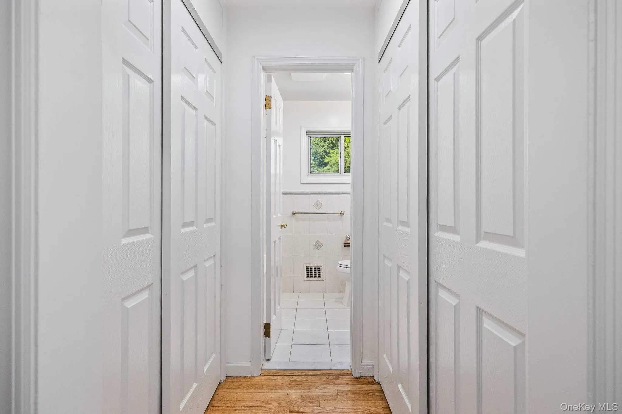 Hall featuring tile walls, light wood finished floors, and a wainscoted wall Hall featuring tile walls, light wood finished floors, and a wainscoted wall