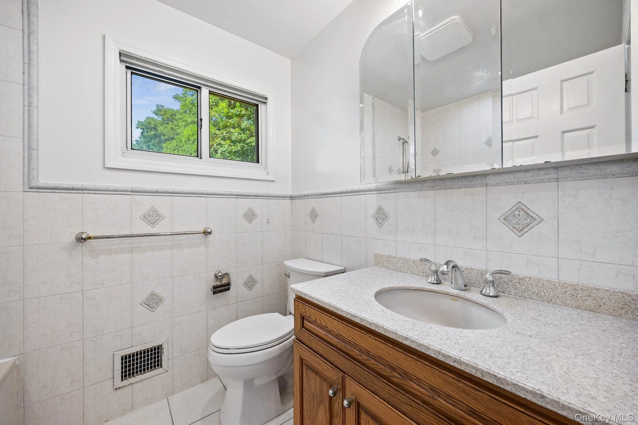 Bathroom featuring vanity, tile walls, tile patterned floors, tiled shower, and a wainscoted wall Bathroom featuring vanity, tile walls, tile patterned floors, tiled shower, and a wainscoted wall