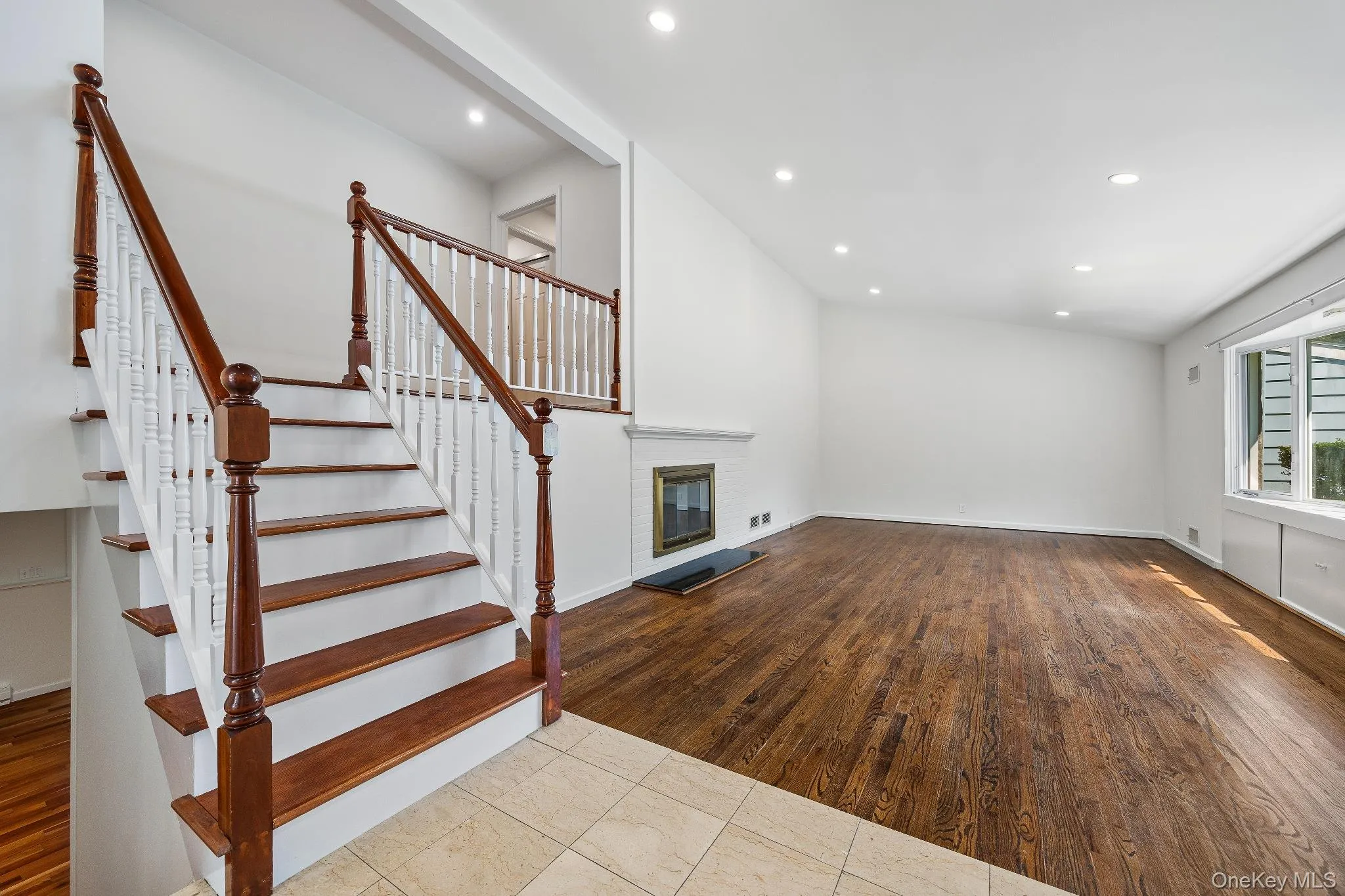 Unfurnished living room with a brick fireplace, recessed lighting, wood finished floors, and stairway Unfurnished living room with a brick fireplace, recessed lighting, wood finished floors, and stairway