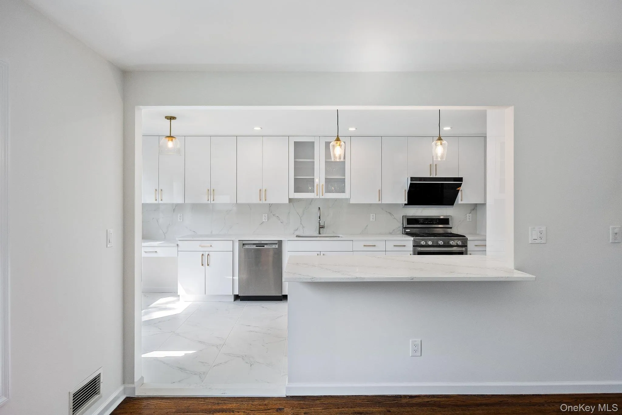 Kitchen with glass insert cabinets, appliances with stainless steel finishes, white cabinets, light stone countertops, and backsplash Kitchen with glass insert cabinets, appliances with stainless steel finishes, white cabinets, light stone countertops, and backsplash