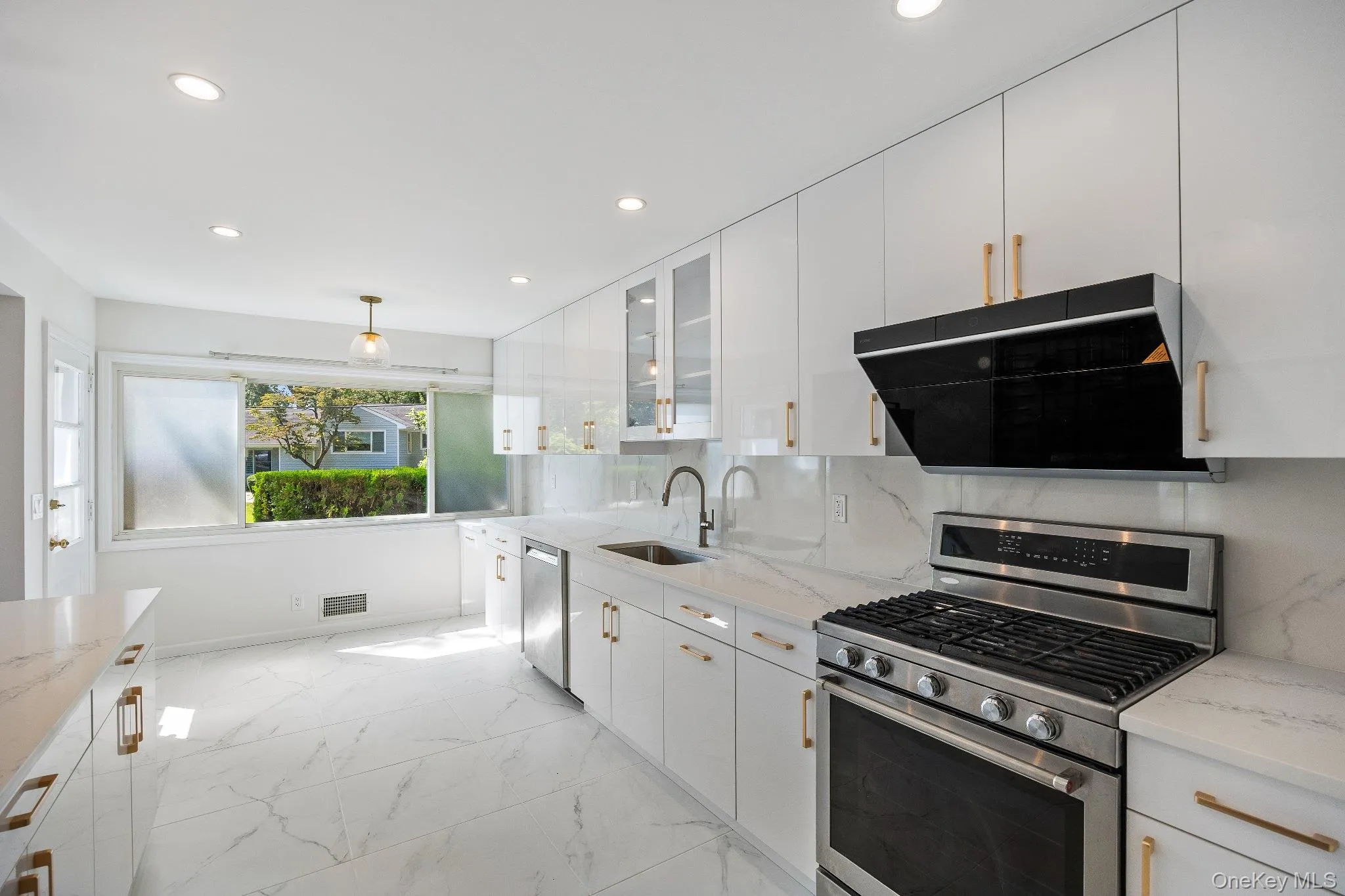 Kitchen with appliances with stainless steel finishes, exhaust hood, light marble finish floors, backsplash, and light stone counters Kitchen with appliances with stainless steel finishes, exhaust hood, light marble finish floors, backsplash, and light stone counters