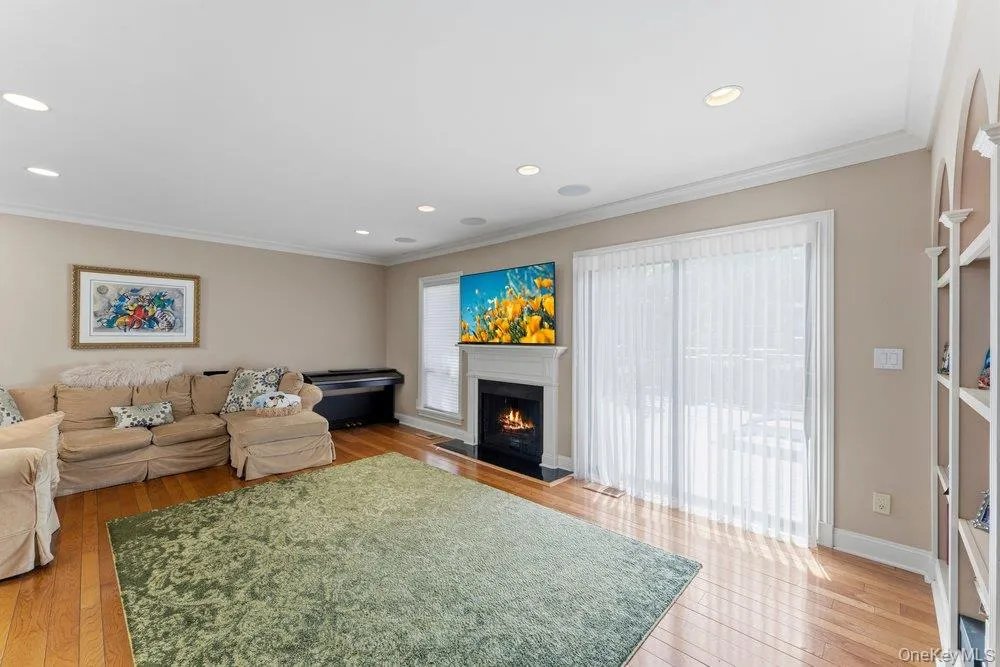 Hardwood flooring throughout featuring a fireplace with a white mantel and dark hearth, built-in recessed lighting, crown molding, and a sliding glass door Hardwood flooring throughout featuring a fireplace with a white mantel and dark hearth, built-in recessed lighting, crown molding, and a sliding glass door
