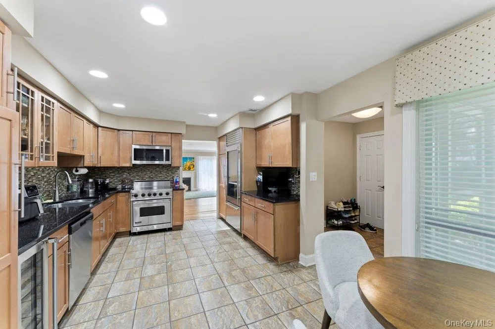 Kitchen featuring wood cabinetry, dark countertops, tiled backsplash, and stainless steel appliances Kitchen featuring wood cabinetry, dark countertops, tiled backsplash, and stainless steel appliances