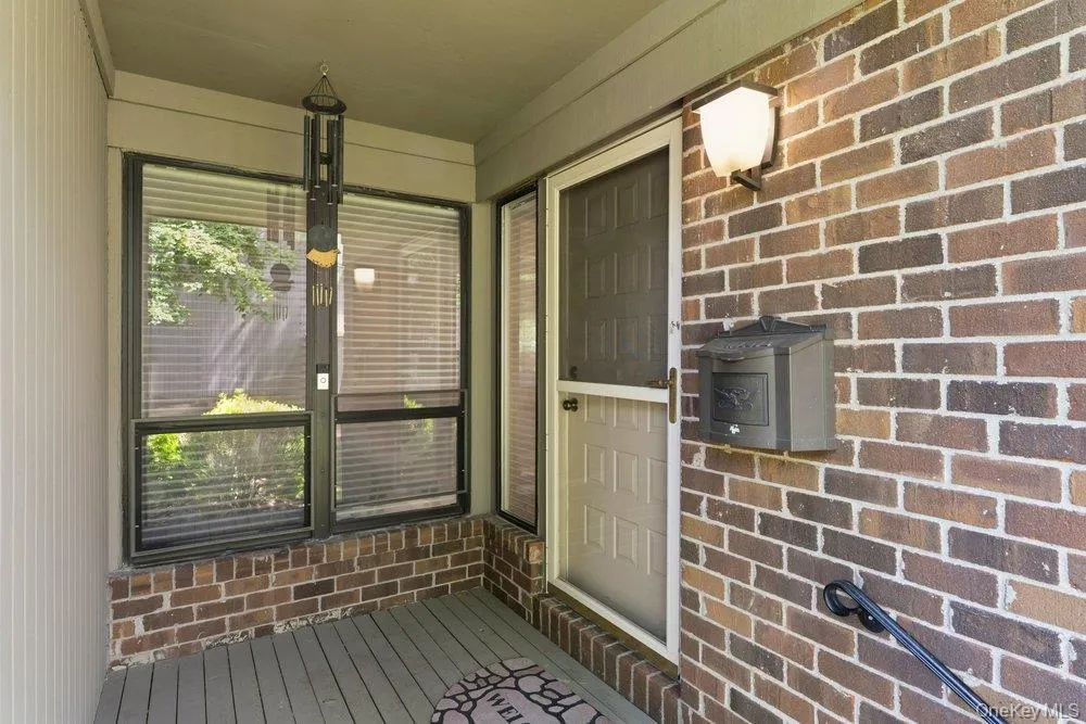 Covered front porch featuring a multi-tone brick exterior, a white entry door with a screen door, and exterior lighting Covered front porch featuring a multi-tone brick exterior, a white entry door with a screen door, and exterior lighting