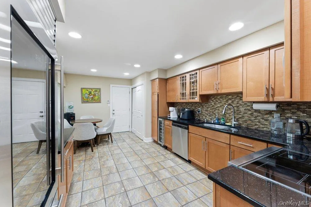 Kitchen featuring wood cabinetry, dark countertops, a mosaic tile backsplash, stainless steel appliances, and tile flooring Kitchen featuring wood cabinetry, dark countertops, a mosaic tile backsplash, stainless steel appliances, and tile flooring