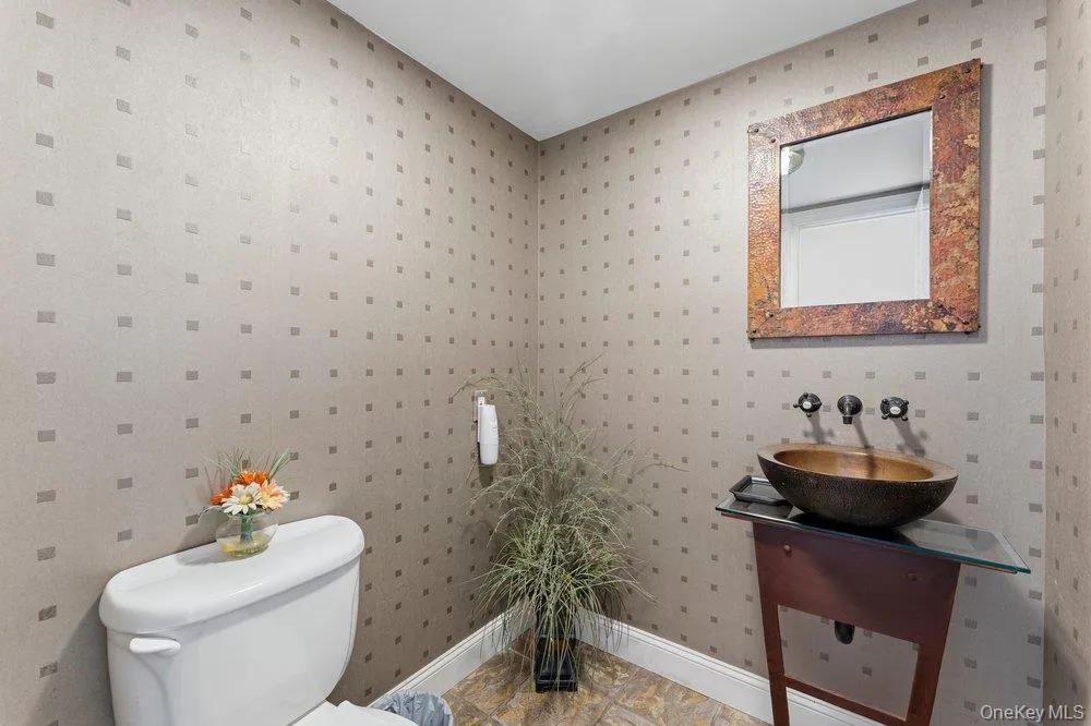 Powder room featuring textured wallpaper, a vessel sink with a wall-mounted faucet, a vanity with a glass top, and tile flooring Powder room featuring textured wallpaper, a vessel sink with a wall-mounted faucet, a vanity with a glass top, and tile flooring