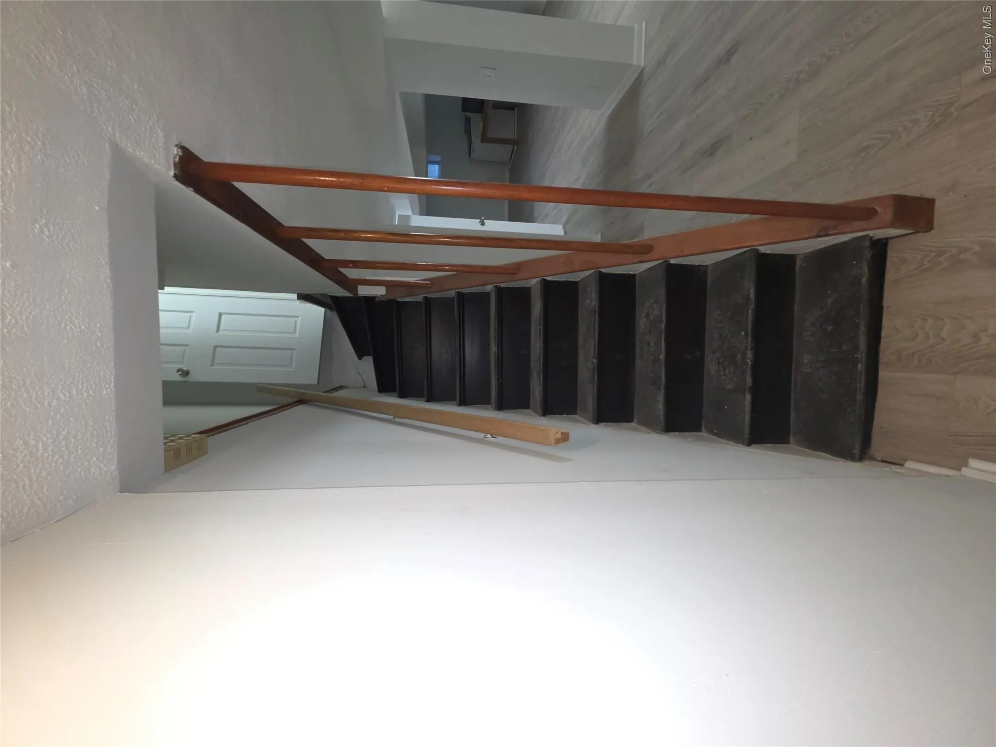 Staircase featuring wood-finish flooring, painted white walls, and a wooden handrail Staircase featuring wood-finish flooring, painted white walls, and a wooden handrail