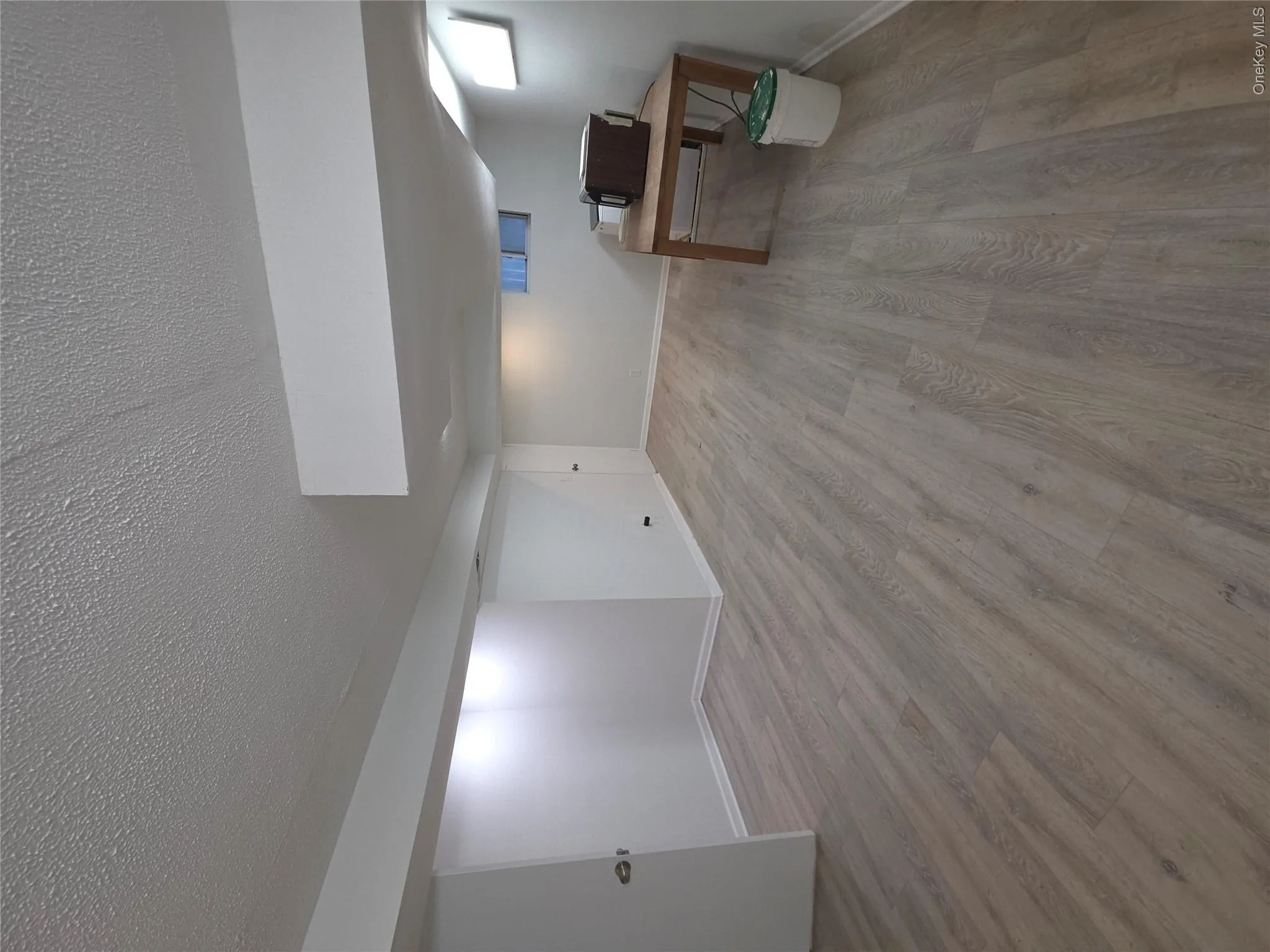 Spacious room featuring light wood-finish flooring, white baseboards, white walls, and a white textured ceiling Spacious room featuring light wood-finish flooring, white baseboards, white walls, and a white textured ceiling