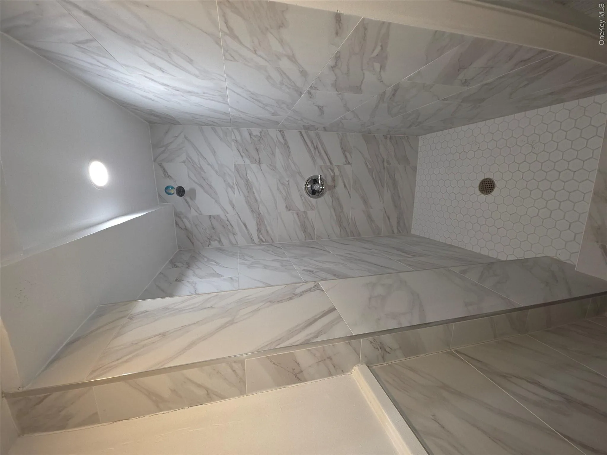 Shower stall with large format marble-look tile walls, hexagonal mosaic tile flooring, and a recessed ceiling light Shower stall with large format marble-look tile walls, hexagonal mosaic tile flooring, and a recessed ceiling light