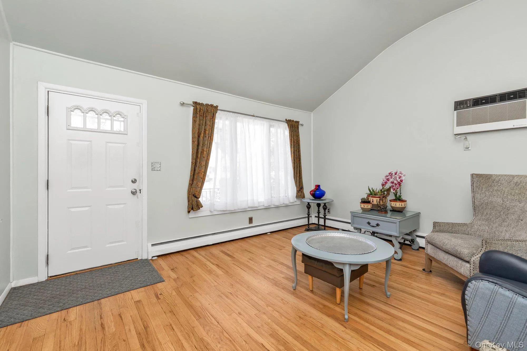 Entry area with wood-finish flooring, a white paneled door with decorative glass inserts, and a wall-mounted air conditioning unit Entry area with wood-finish flooring, a white paneled door with decorative glass inserts, and a wall-mounted air conditioning unit