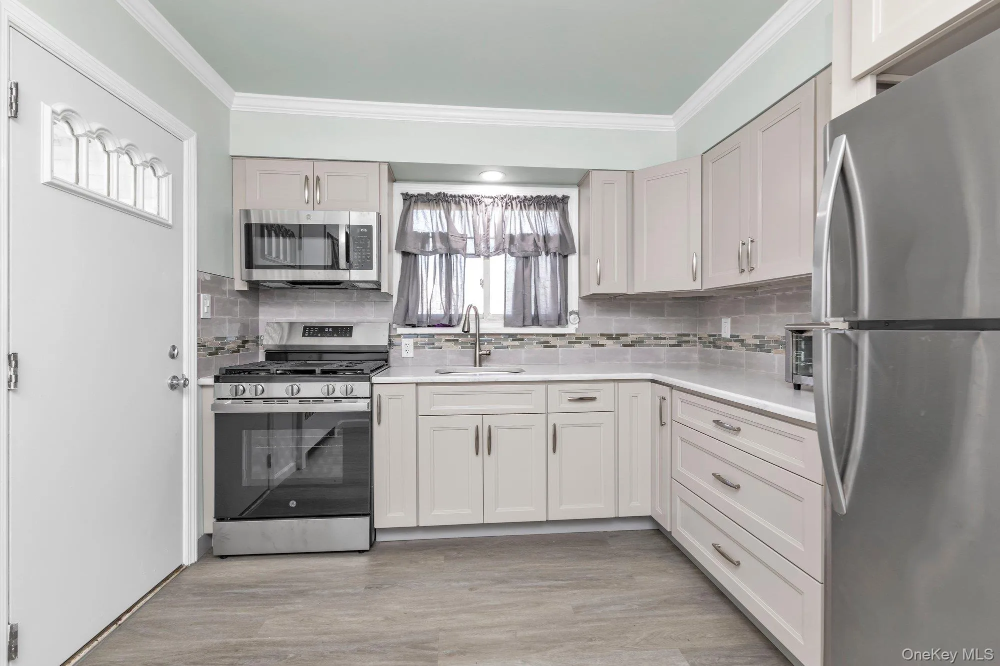 Modern kitchen featuring light-toned cabinetry, stainless steel appliances, a tiled backsplash, and light countertops Modern kitchen featuring light-toned cabinetry, stainless steel appliances, a tiled backsplash, and light countertops