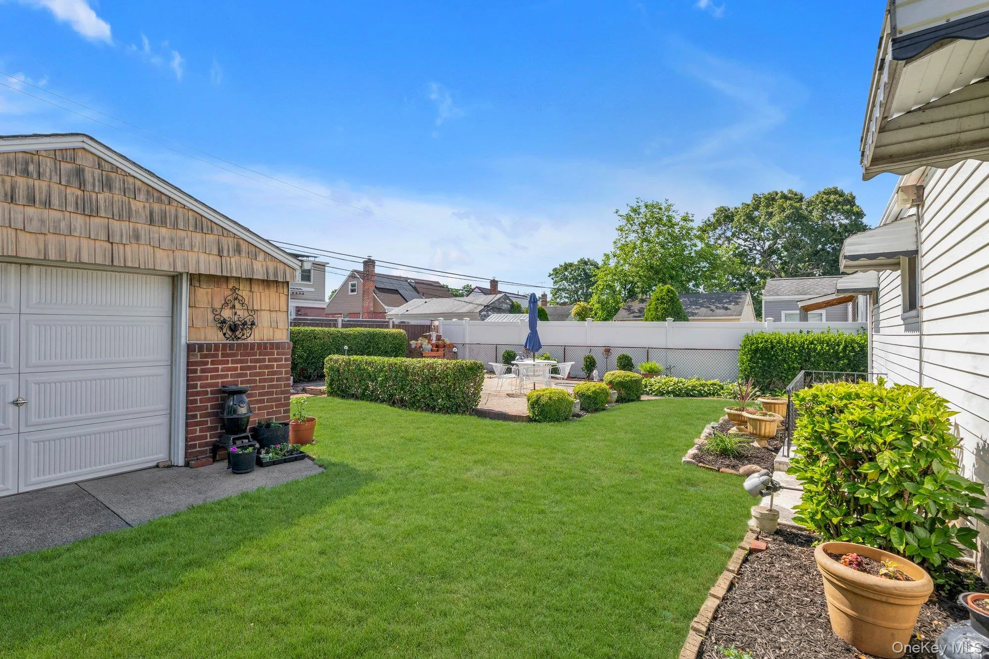 Spacious backyard featuring a manicured lawn, established landscaping, and a brick patio Spacious backyard featuring a manicured lawn, established landscaping, and a brick patio