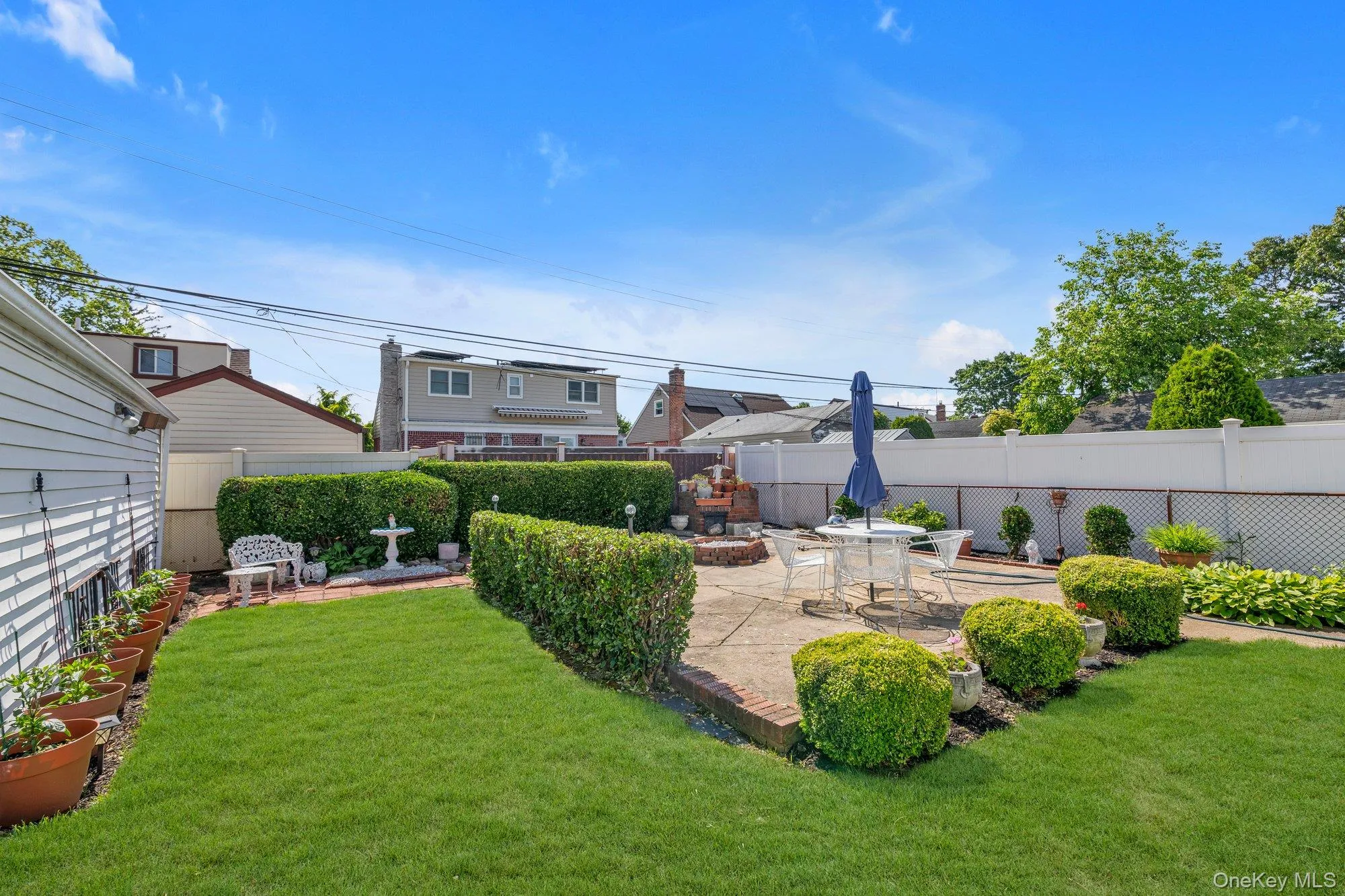 Expansive backyard featuring a stone patio, manicured lawn, and mature hedges Expansive backyard featuring a stone patio, manicured lawn, and mature hedges