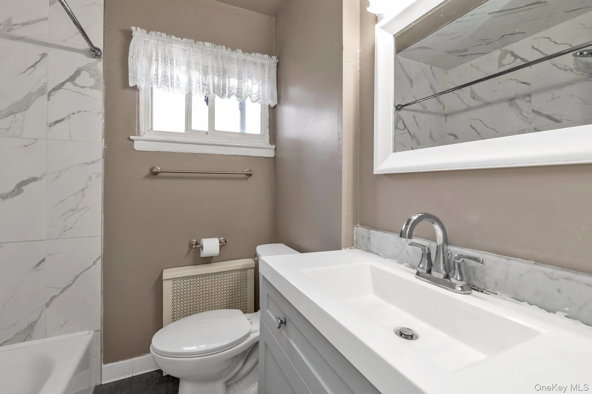 Bathroom featuring a single vanity with an integrated sink, chrome faucet, and framed mirror Bathroom featuring a single vanity with an integrated sink, chrome faucet, and framed mirror