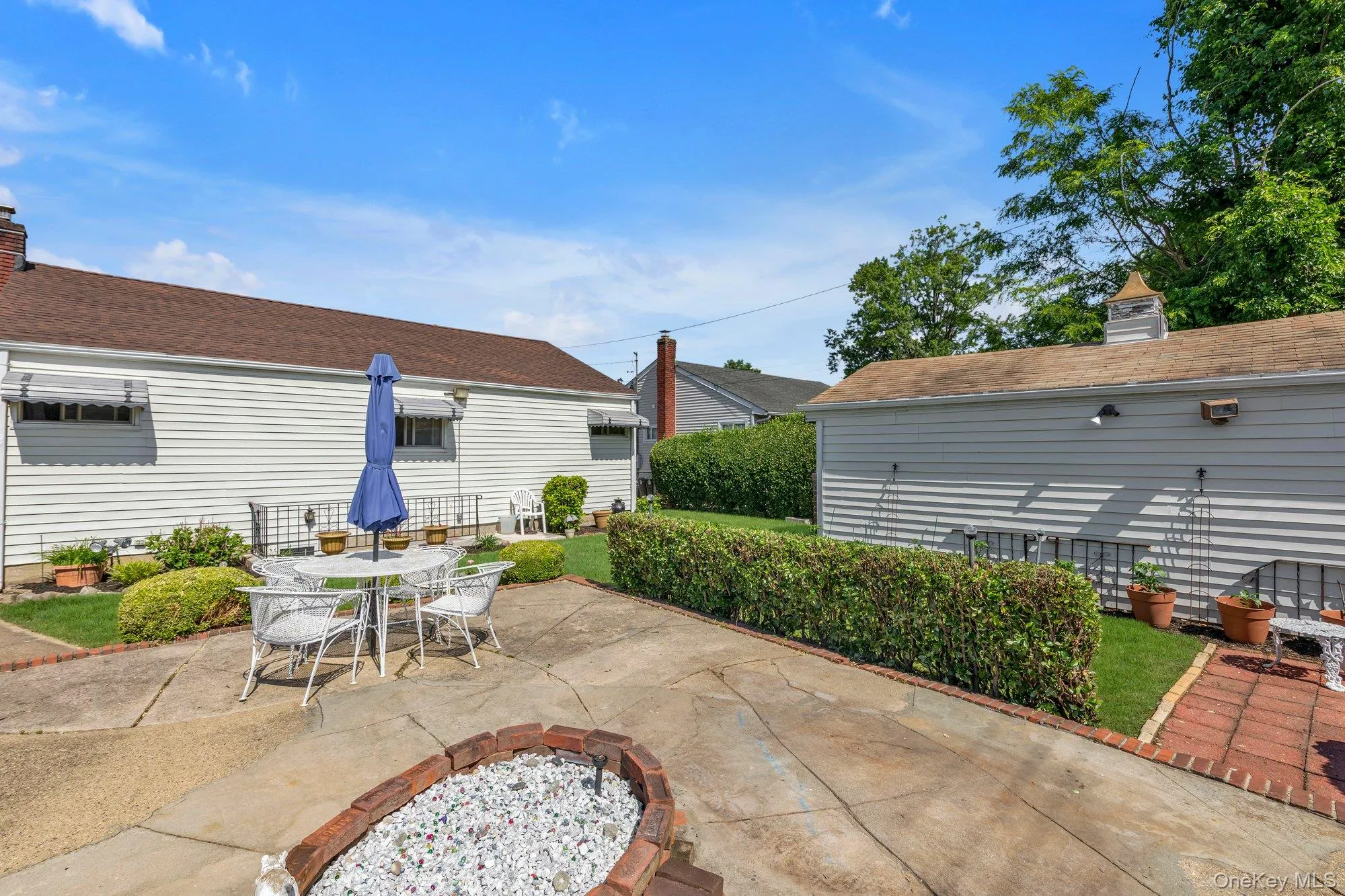 Backyard featuring a concrete patio, brick-edged fire pit area, and manicured lawn Backyard featuring a concrete patio, brick-edged fire pit area, and manicured lawn