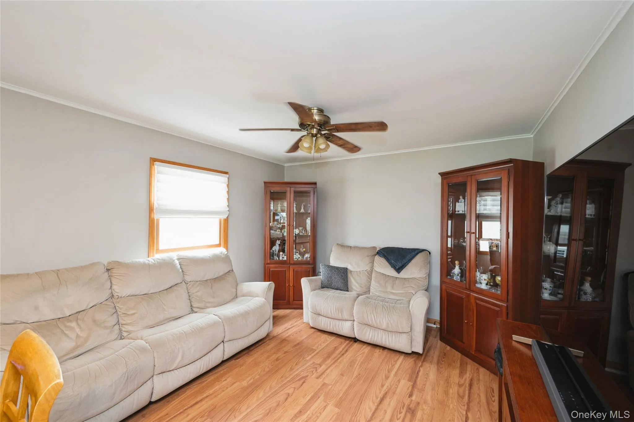 Hardwood-finish flooring throughout the room features a ceiling fan with integrated lighting, crown molding, and a window with white blinds Hardwood-finish flooring throughout the room features a ceiling fan with integrated lighting, crown molding, and a window with white blinds