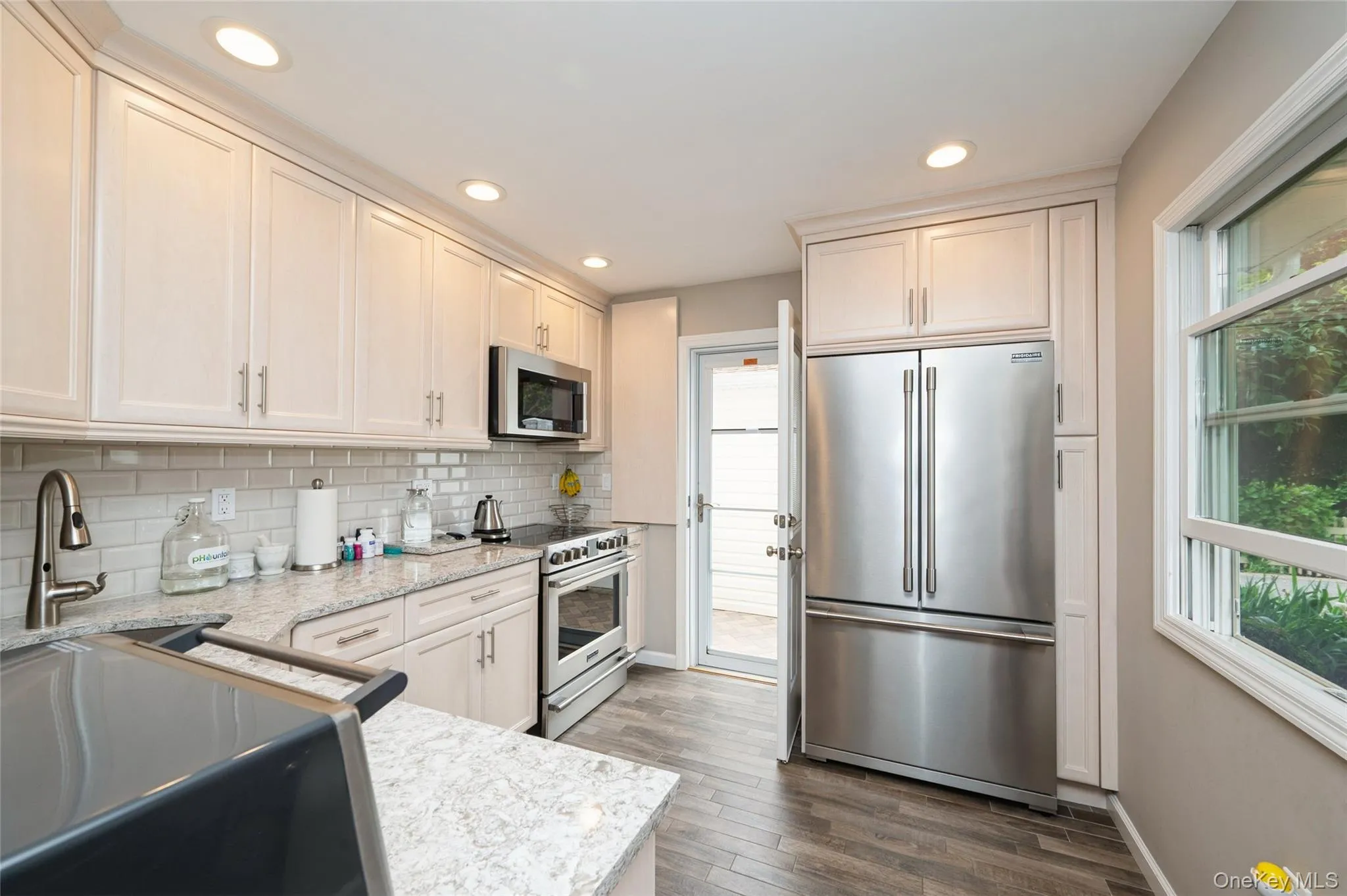 Kitchen featuring light-toned cabinetry, light granite-style countertops, stainless steel appliances, wood-finish flooring, and recessed lighting Kitchen featuring light-toned cabinetry, light granite-style countertops, stainless steel appliances, wood-finish flooring, and recessed lighting