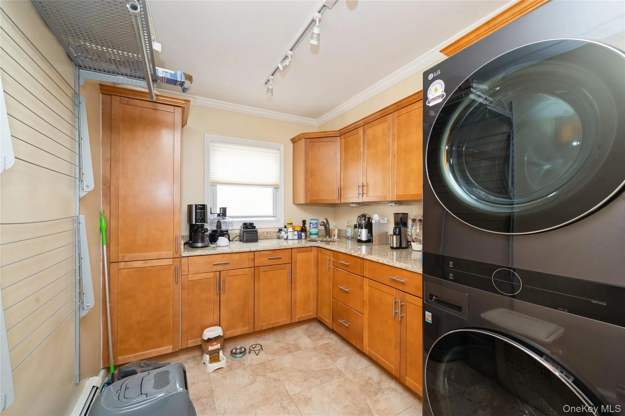 Pantry/Laundry area featuring a stacked washer and dryer, wood-finish cabinetry, light-toned countertop, and tiled flooring Pantry/Laundry area featuring a stacked washer and dryer, wood-finish cabinetry, light-toned countertop, and tiled flooring