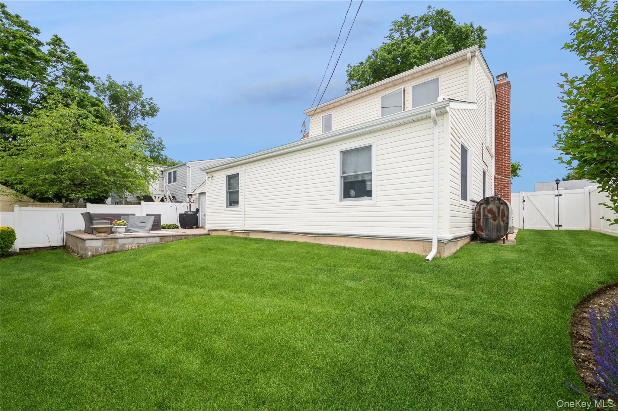Rear exterior featuring white vinyl siding, a brick chimney, and a white vinyl fence enclosing the yard Rear exterior featuring white vinyl siding, a brick chimney, and a white vinyl fence enclosing the yard
