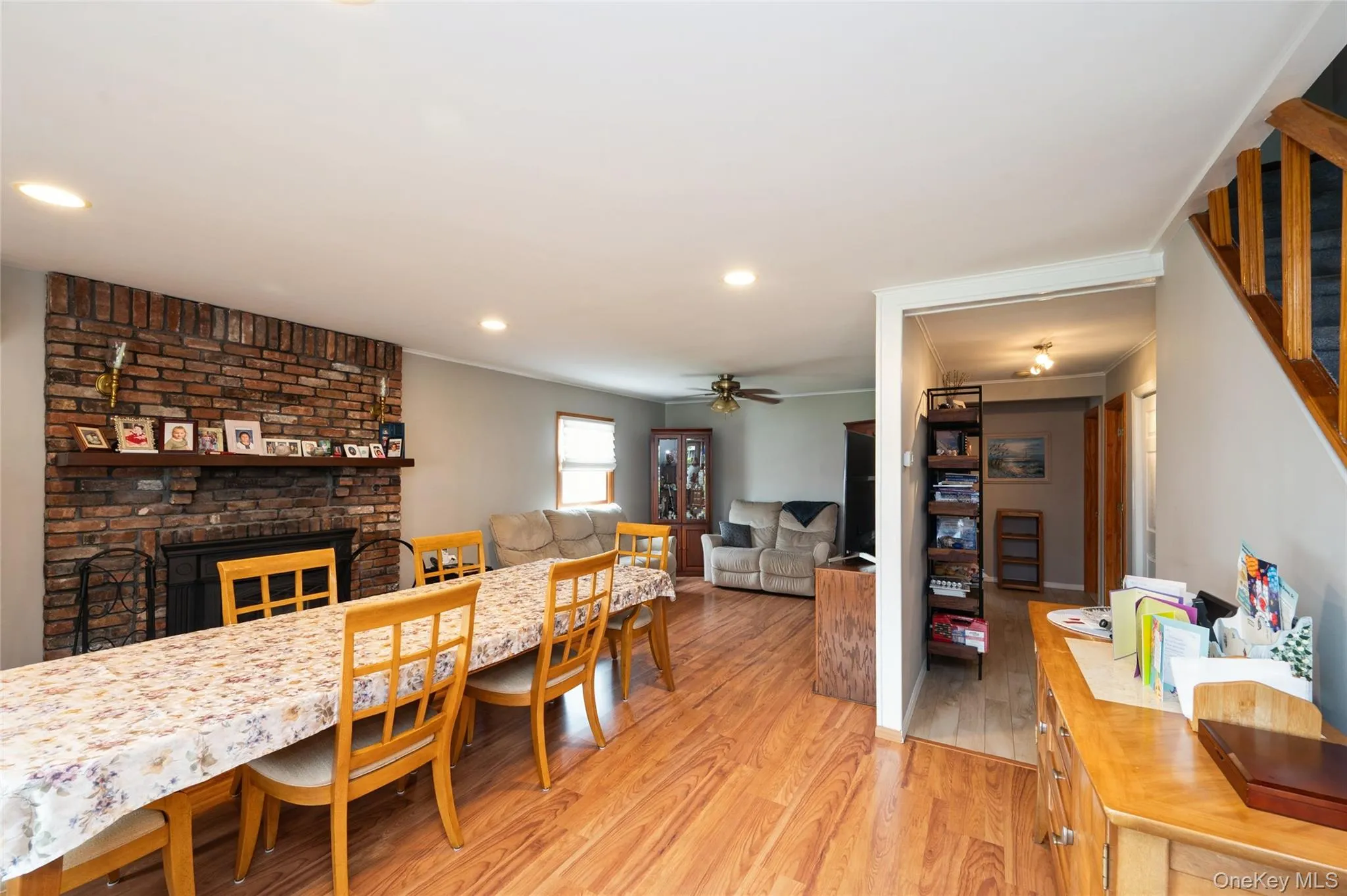 Open concept living space featuring wood-finish flooring, a brick fireplace with a mantel, recessed lighting, a ceiling fan, and a wood staircase Open concept living space featuring wood-finish flooring, a brick fireplace with a mantel, recessed lighting, a ceiling fan, and a wood staircase